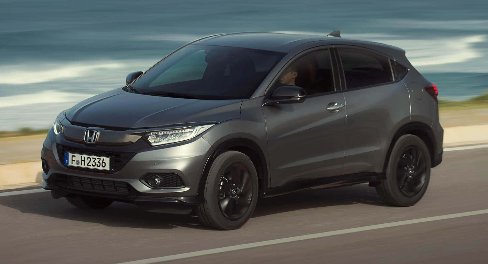 Honda Hr-v 桌布 壁紙 — 一輛時尚的灰色本田HR-V沿著海岸公路行駛，背景是模糊的海浪。