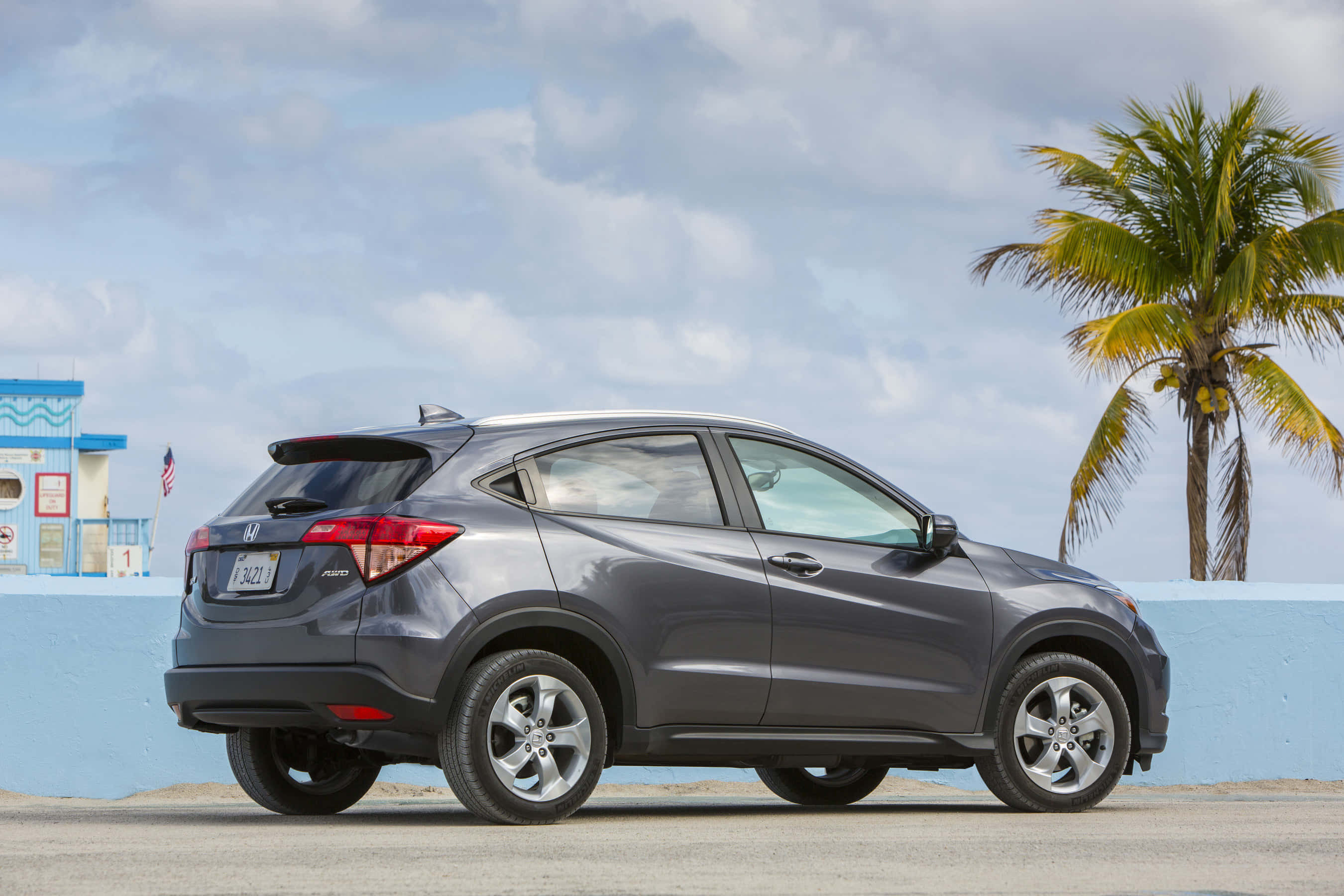 Honda Hr-v 桌布 壁紙 — 一架時尚的灰色本田 HR-V 停泊在棕櫚樹旁，天空局部多雲，靠近一棟藍色建築物。