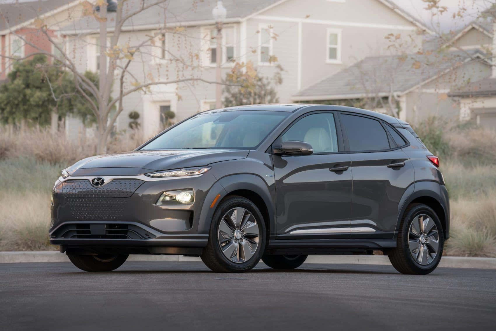 Hyundai Kona 桌布 壁紙 — 一架時尚灰色Hyundai Kona EV停泊在郊區街道上，背景有房屋和乾草。