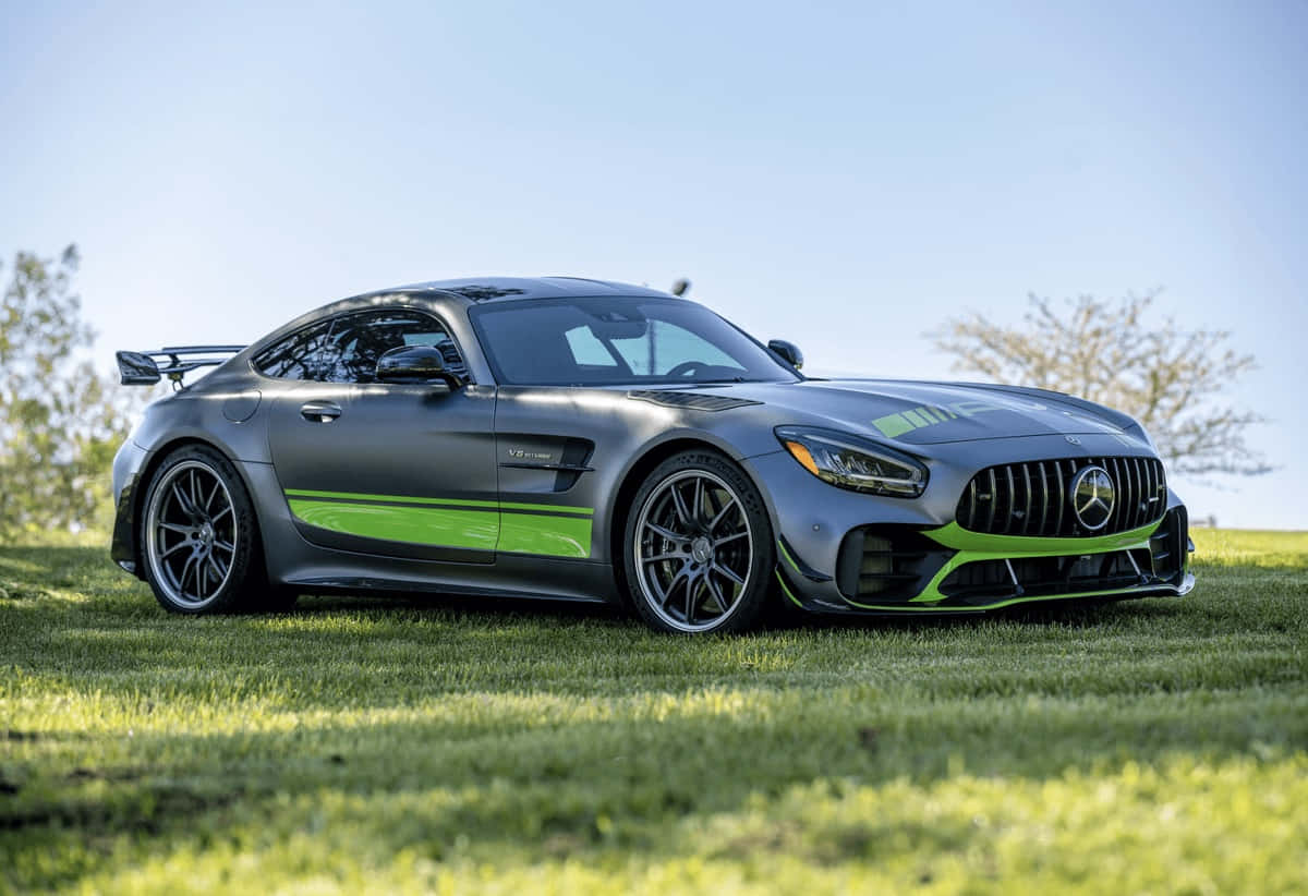  壁紙 — 一輛時尚的灰色Mercedes-AMG GT R帶有鮮綠色點綴，停放在陽光明媚的草地上，背景是清澈的藍天。