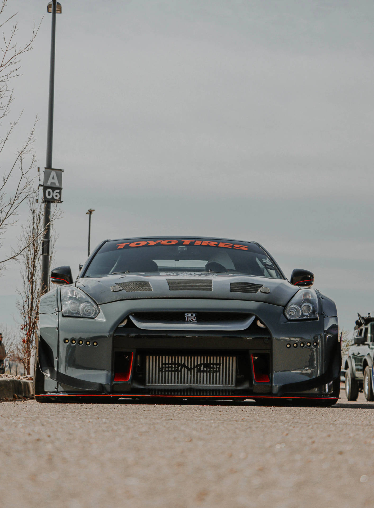 灰色日產GT-R賽車，帶有紅色飾邊，停泊在陰天下的瀝青路面上。
