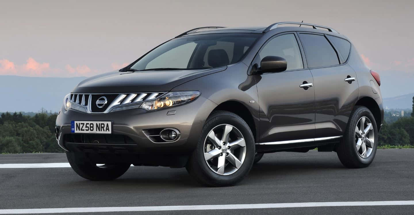 Nissan Murano 桌布 壁紙 — 一輛時尚的灰色日產Murano SUV停在瀝青路上，遠處是樹木成行的地平線，天空柔和暮色。