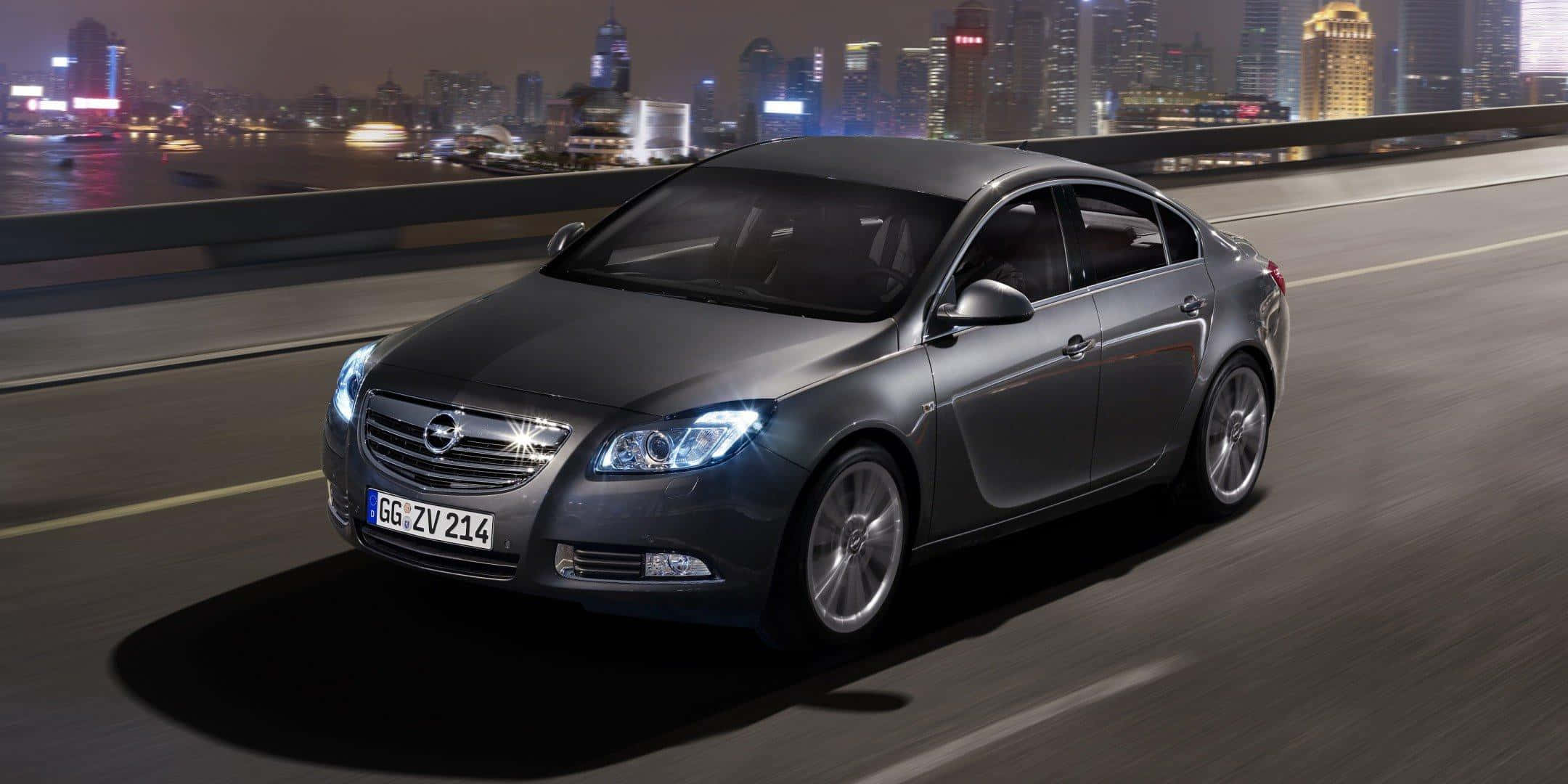 Opel Insignia 桌布 壁紙 — 一架時尚灰色房車在夜間高速駛過橋樑，背景是閃爍的活力城市天際線。