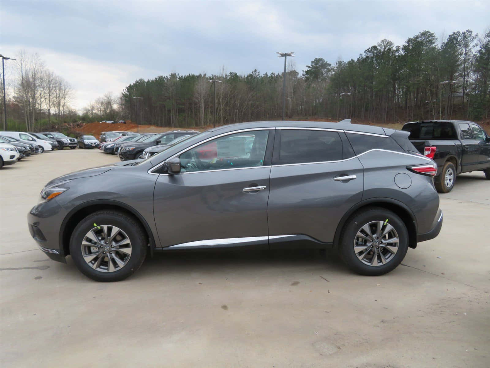 Nissan Murano 桌布 壁紙 — 一輛時尚的灰色SUV停泊在一個有樹木和其他車輛的停車場，天空多雲。