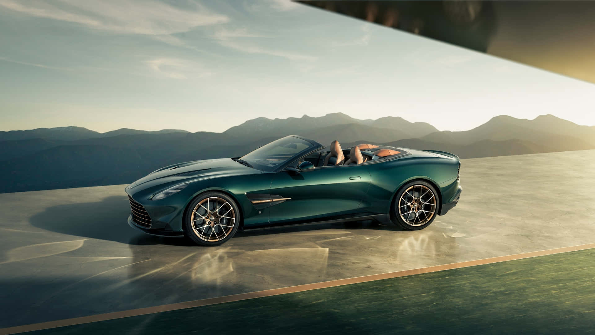  壁紙 — 一架時尚的綠色Aston Martin DB12 Volante開篷跑車停泊在陽光普照的混凝土平台上，背景是山脈。