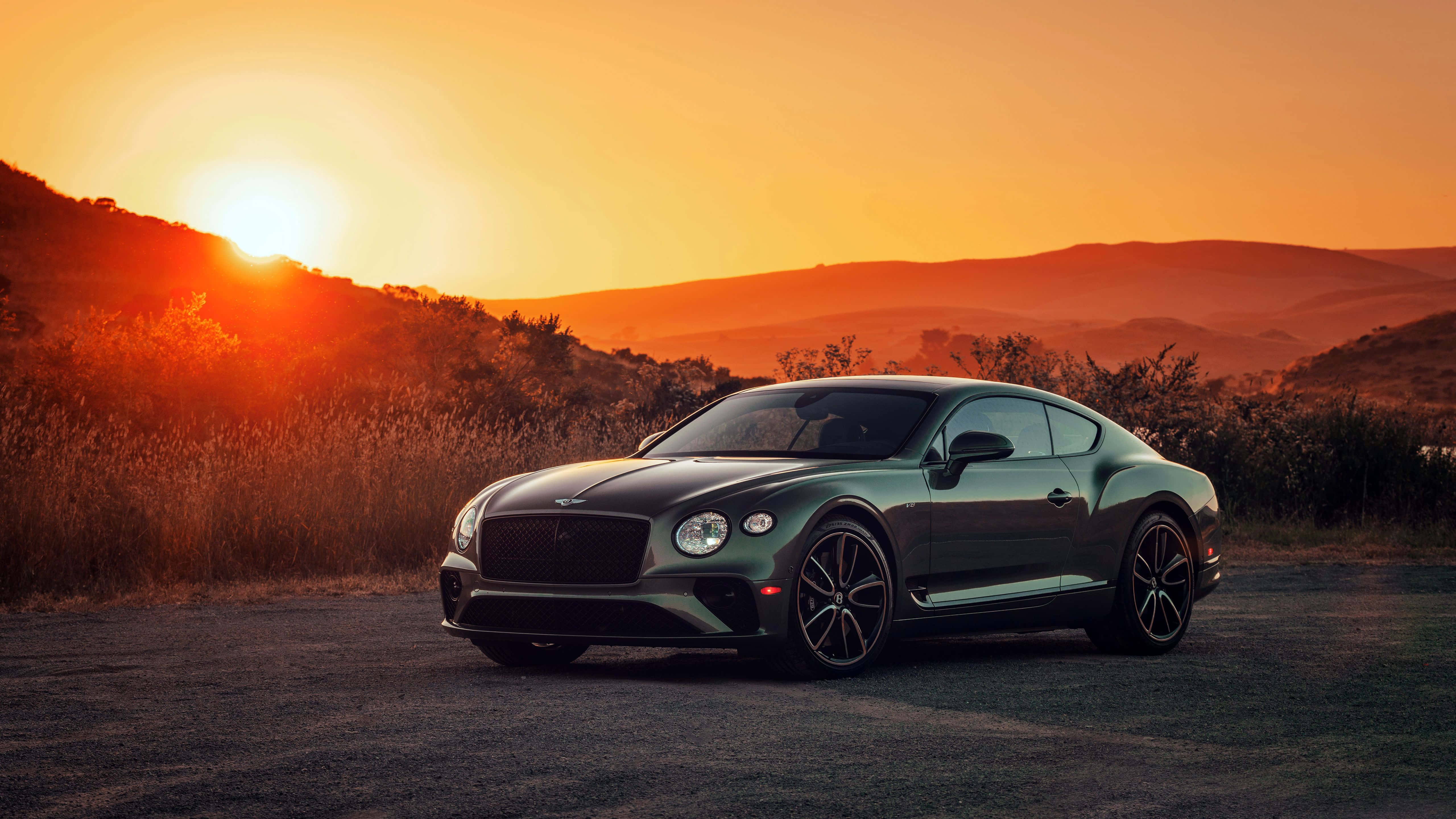 Bentley Continental Gt 桌布 壁紙 — 一輛時尚的綠色賓利 Continental GT 停在日落時分的道路上，起伏的山丘沐浴在金色光芒中。