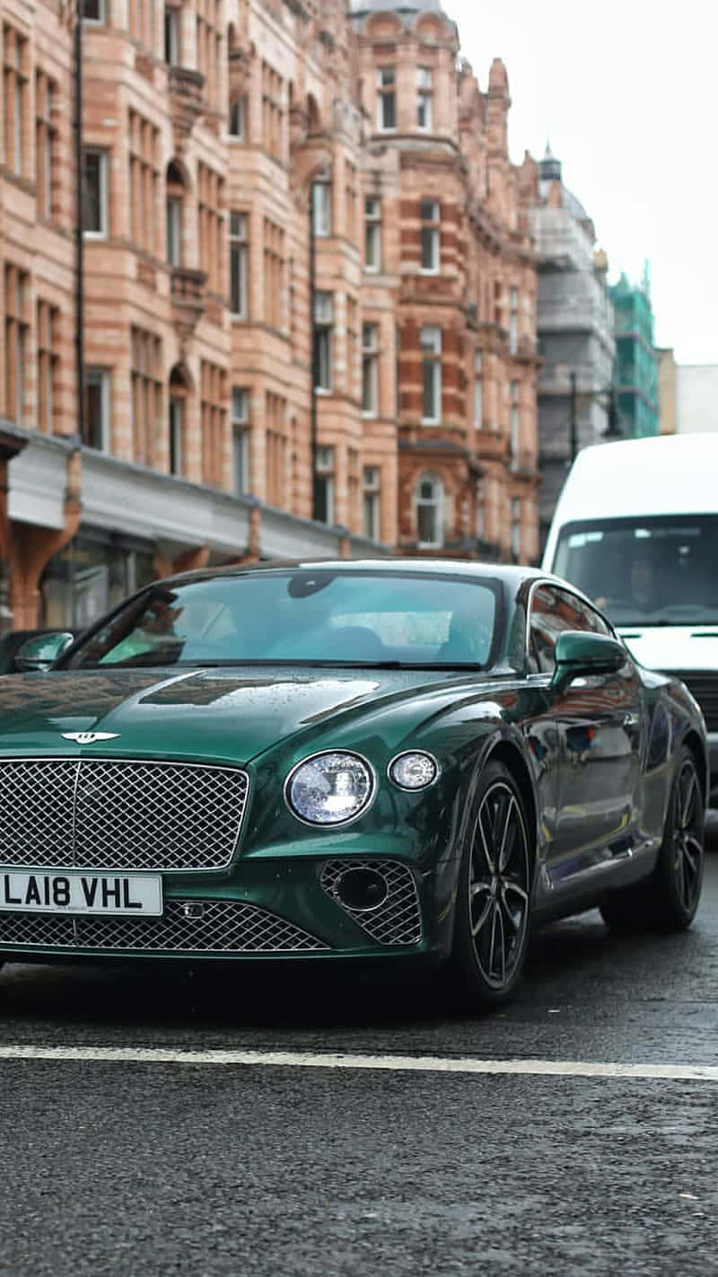 Bentley Continental Gt 桌布 壁紙 — 一輛時尚的綠色賓利 Continental GT 停在潮濕的城市街道上，旁邊是華麗的磚砌建築。