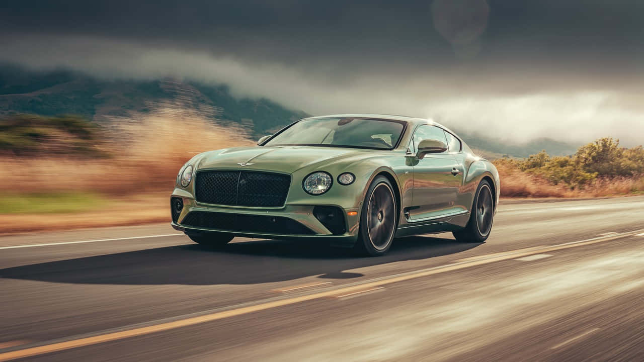 Bentley Continental Gt 桌布 壁紙 — 一輛時尚的綠色賓利 Continental GT 在沙漠公路上疾馳，帶有模糊的動感和戲劇性的多雲天空。