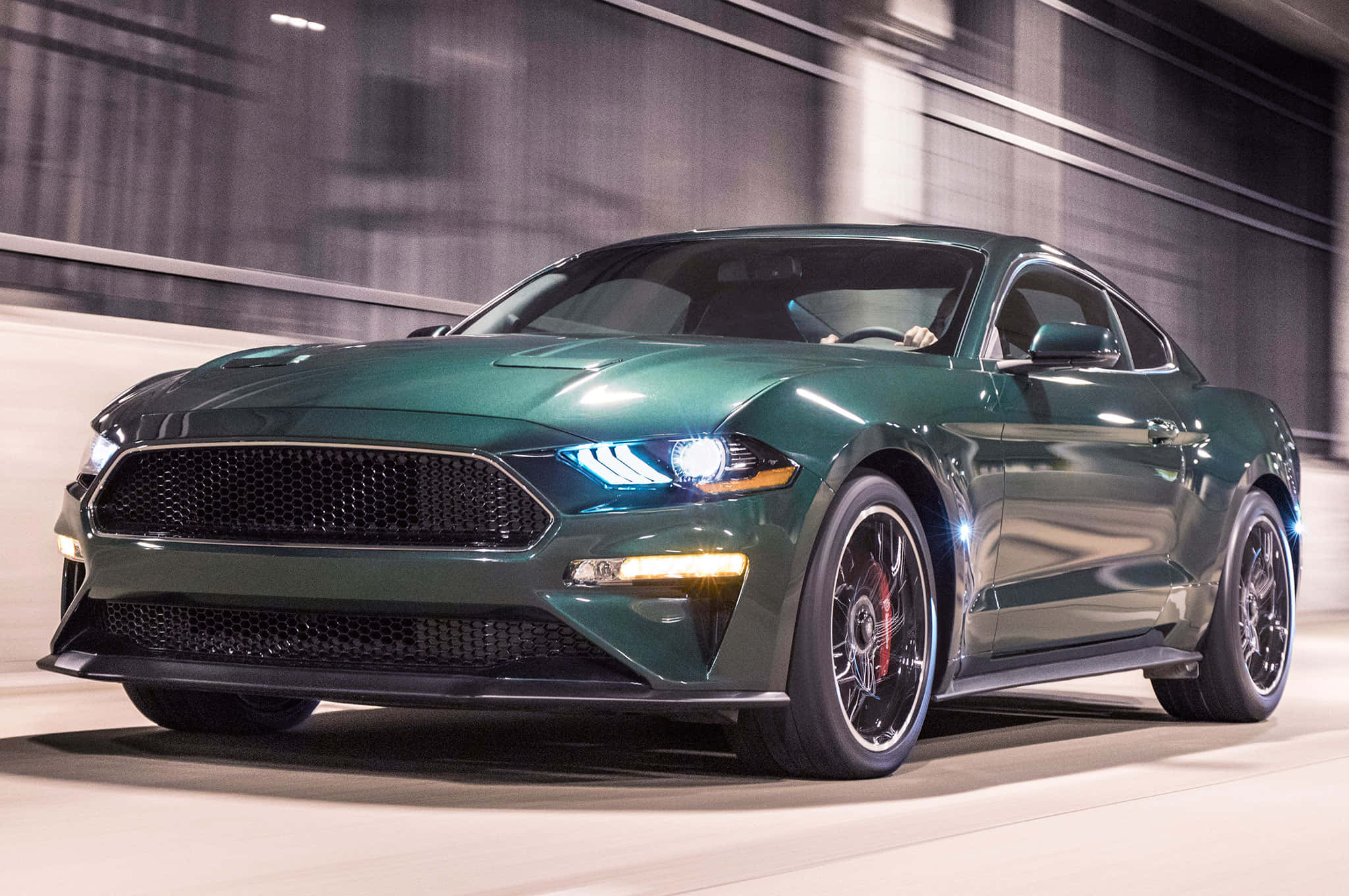 Ford Mustang Bullitt 桌布 壁紙 — 一輛時尚的綠色福特野馬在現代隧道中疾馳，車頭燈閃爍，背景呈現動態模糊效果。