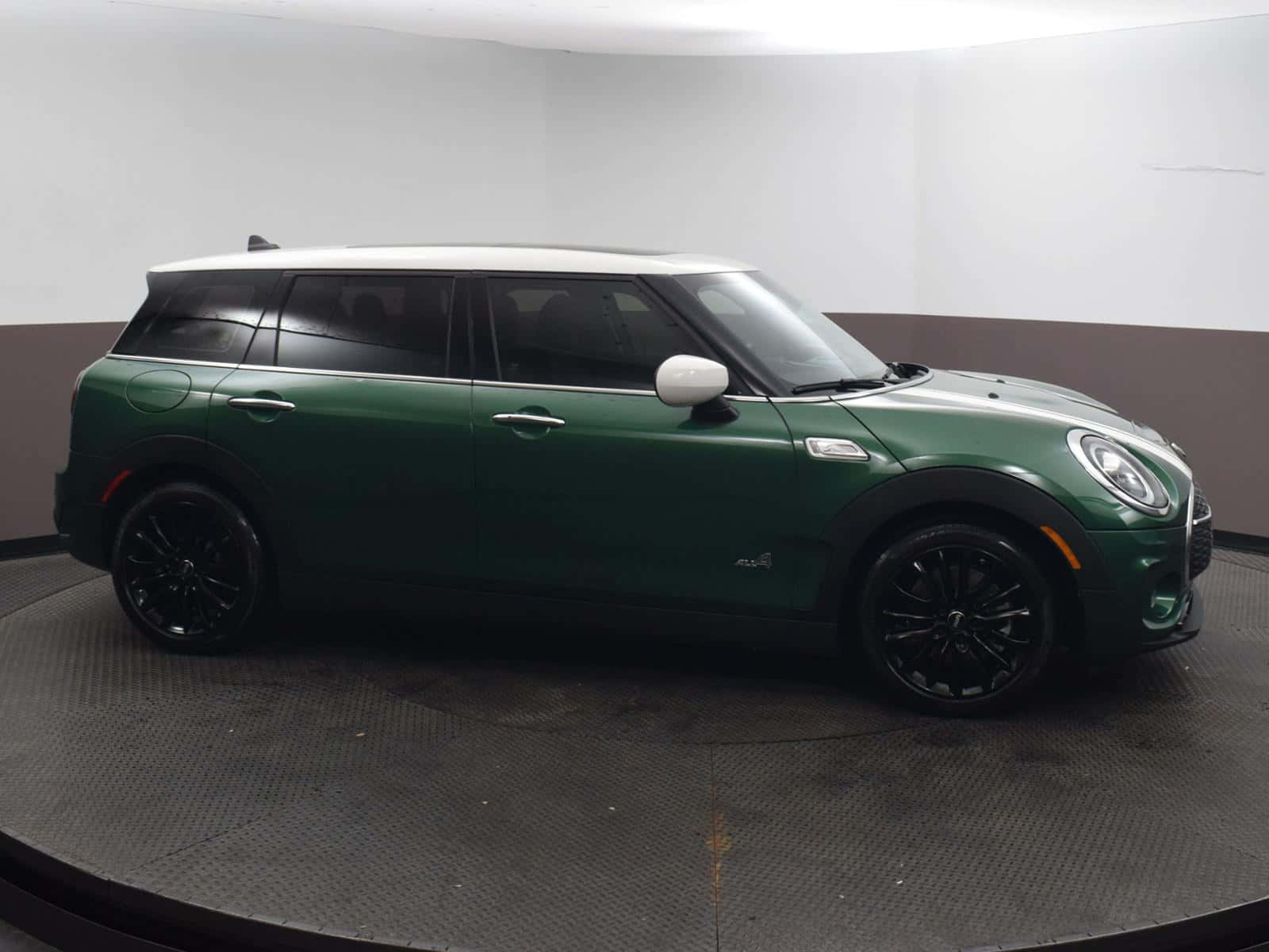 Mini Cooper S Clubman All4 桌布 壁紙 — 一輛時尚的綠色MINI Countryman配備黑色輪圈，位於簡約工作室空間中的旋轉平台中央。