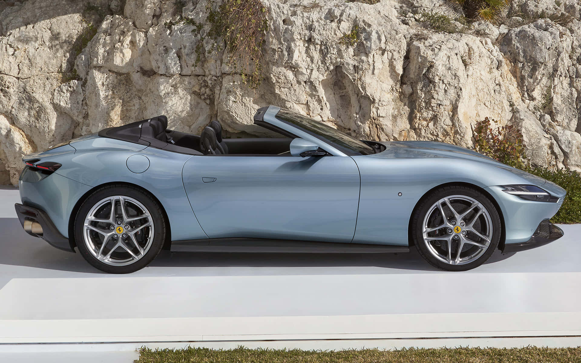 Ferrari Roma 桌布 壁紙 — 一架時尚的淺藍色法拉利開篷車停泊在白色平台上，背景是崎嶇的岩石懸崖。