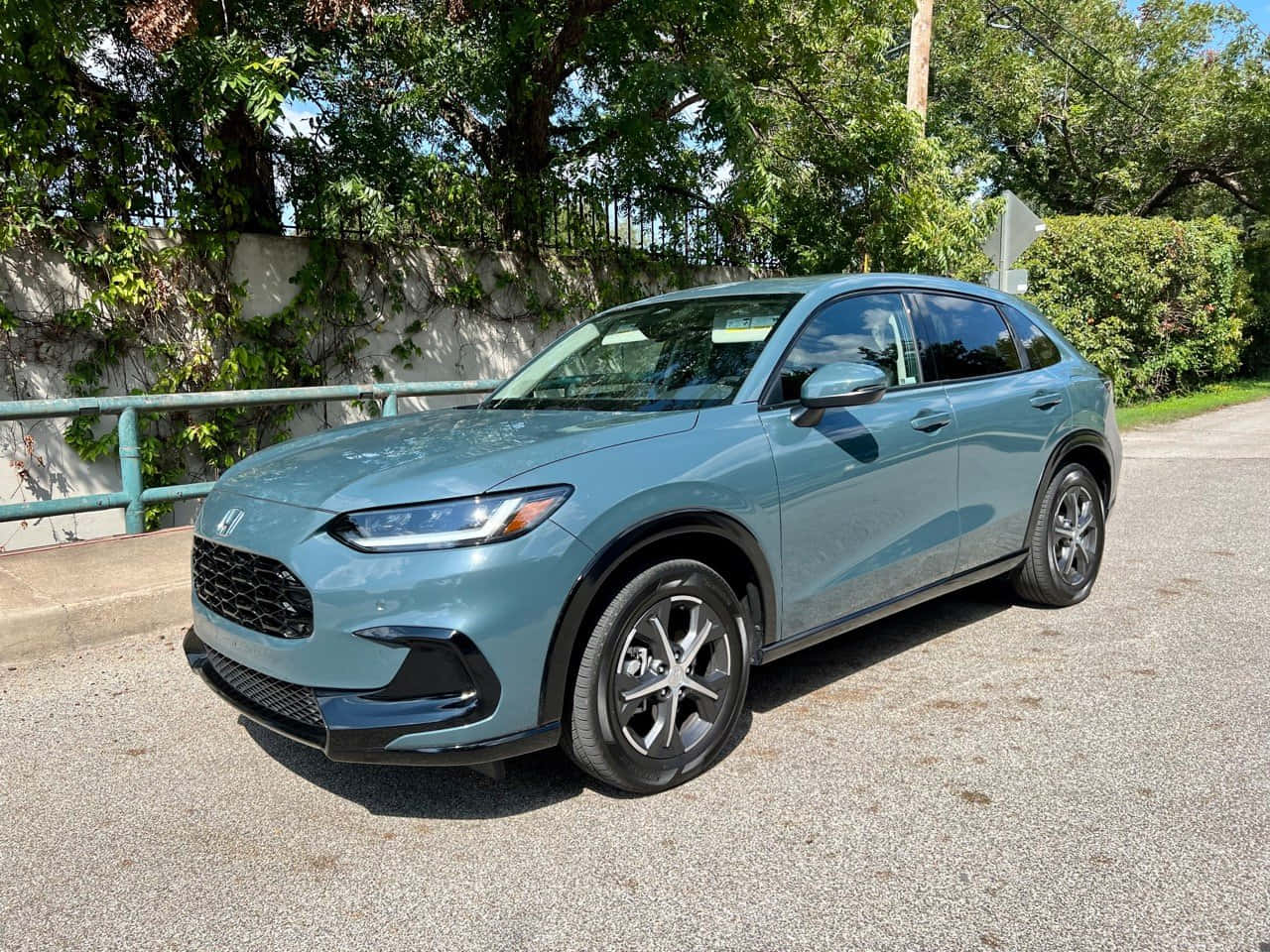 Honda Hr-v 桌布 壁紙 — 一輛時尚的淺藍色本田SUV停在碎石車道上，旁邊是綠色圍欄和枝葉茂密的樹木，在明亮的日光下。