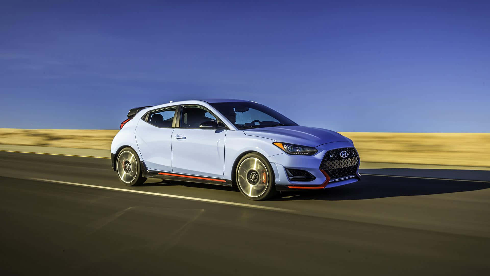 Hyundai Veloster 桌布 壁紙 — 一輛時尚的淺藍色Hyundai Veloster N在晴朗藍天下沿沙漠高速公路奔馳，帶有動態模糊效果。