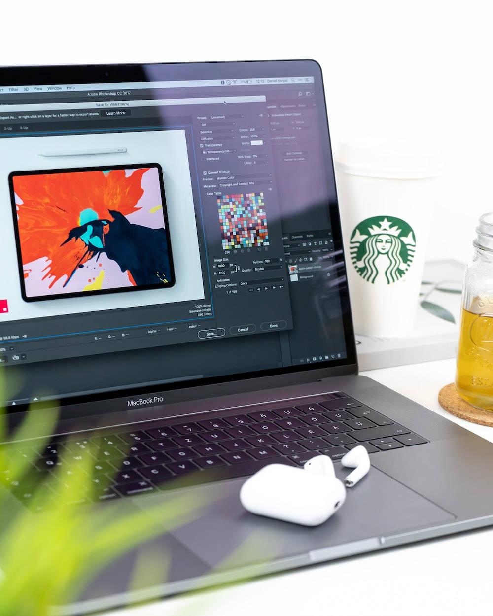 MacBook Pro 打開數位藝術，旁邊放著咖啡和耳塞，在乾淨的桌子上。