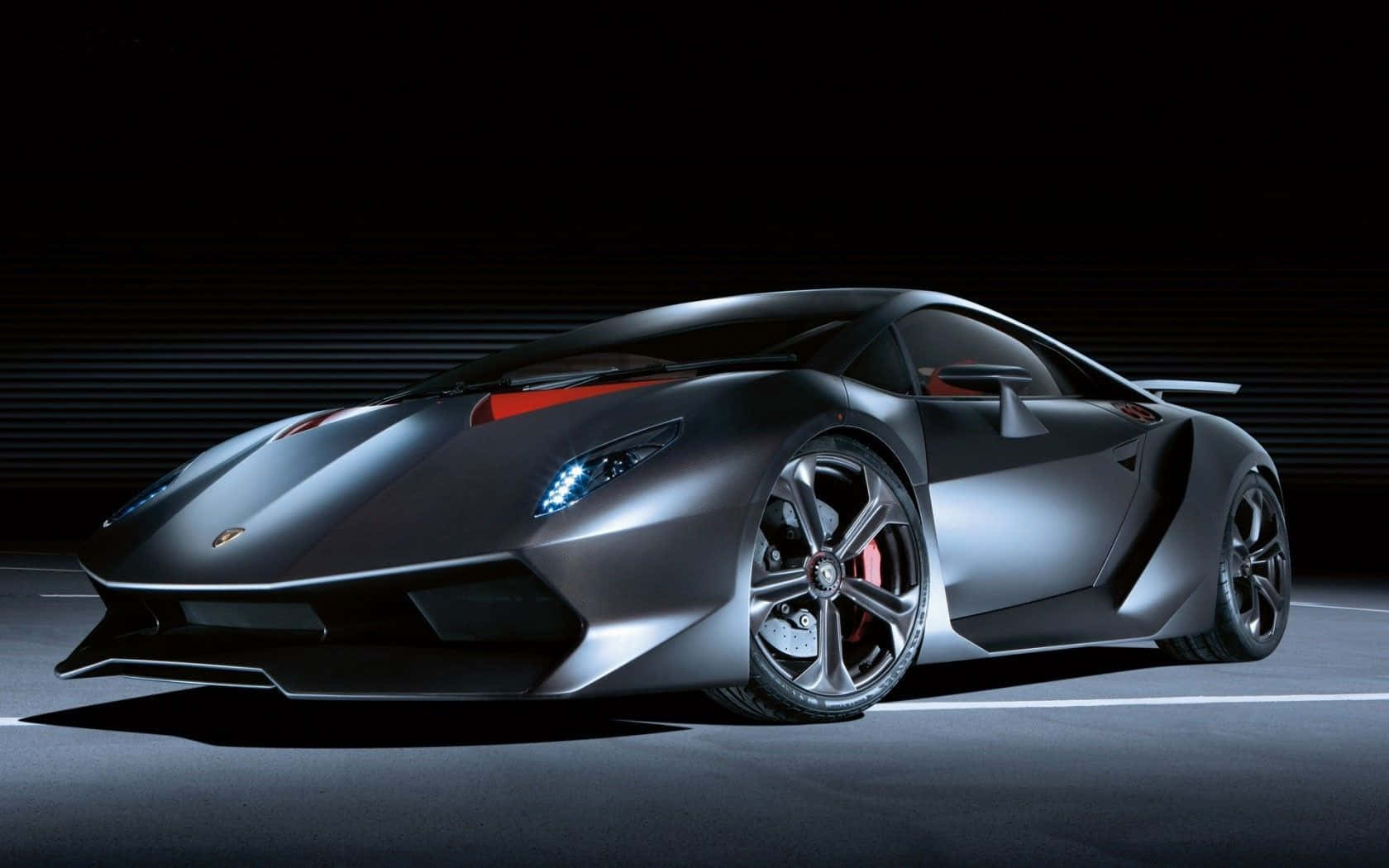Lamborghini Sesto Elemento 桌布 壁紙 — 一輛時尚的啞光黑色林寶堅尼跑車，帶有發光的藍色車頭燈和紅色點綴，在黑暗的攝影棚背景下戲劇性地照亮。