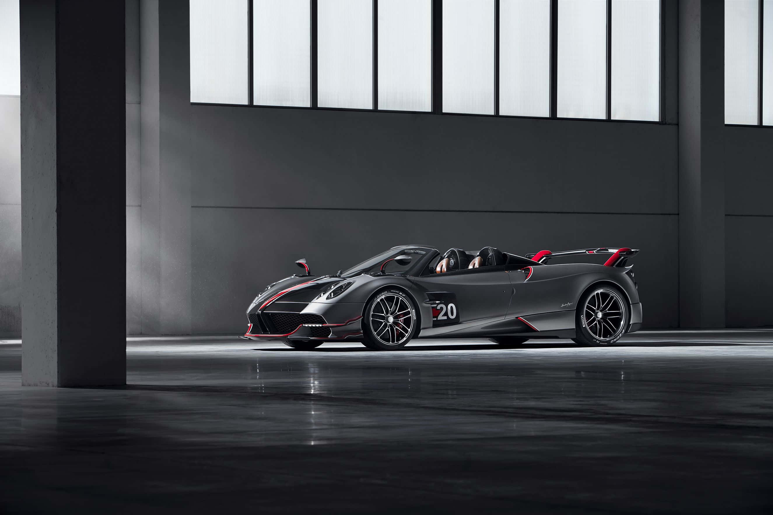 Pagani Huayra Roadster Bc 桌布 壁紙 — 一輛時尚的啞光黑色帕加尼 Huayra Roadster 帶有紅色點綴，在工業照明下於簡約混凝土車庫中閃耀。