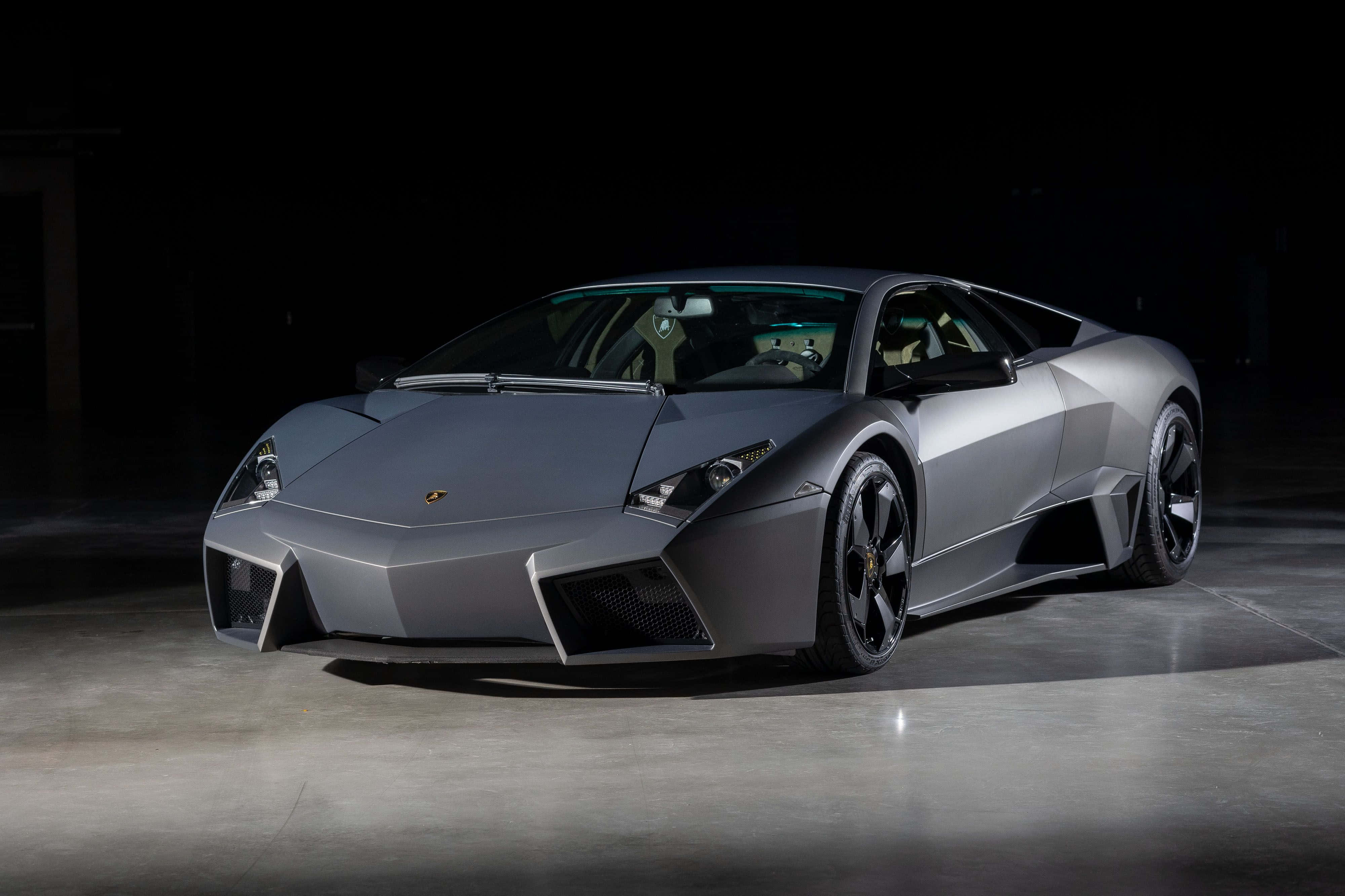 Lamborghini Reventón 桌布 壁紙 — 一輛時尚的啞光灰色林寶堅尼Reventon跑車在黑暗的攝影棚背景下被戲劇性地照亮。