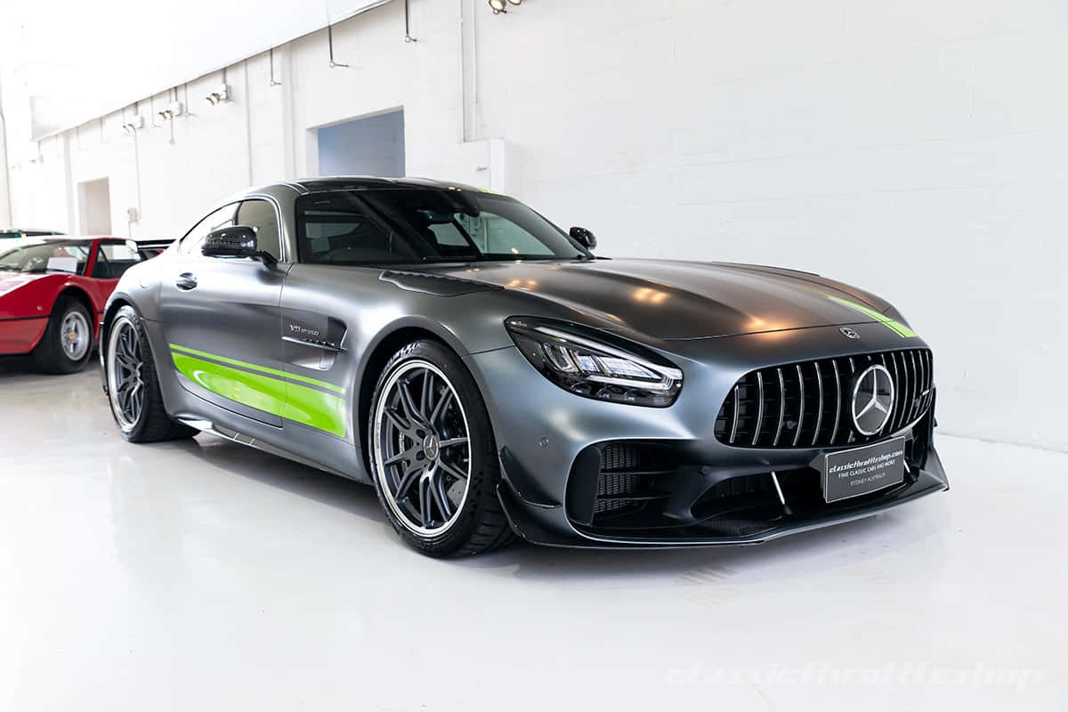  壁紙 — 一輛光滑的啞光灰色Mercedes-AMG GT，帶有充滿活力的綠色賽車條紋，在明亮的攝影棚燈光下，於潔白的車庫中閃閃發光。