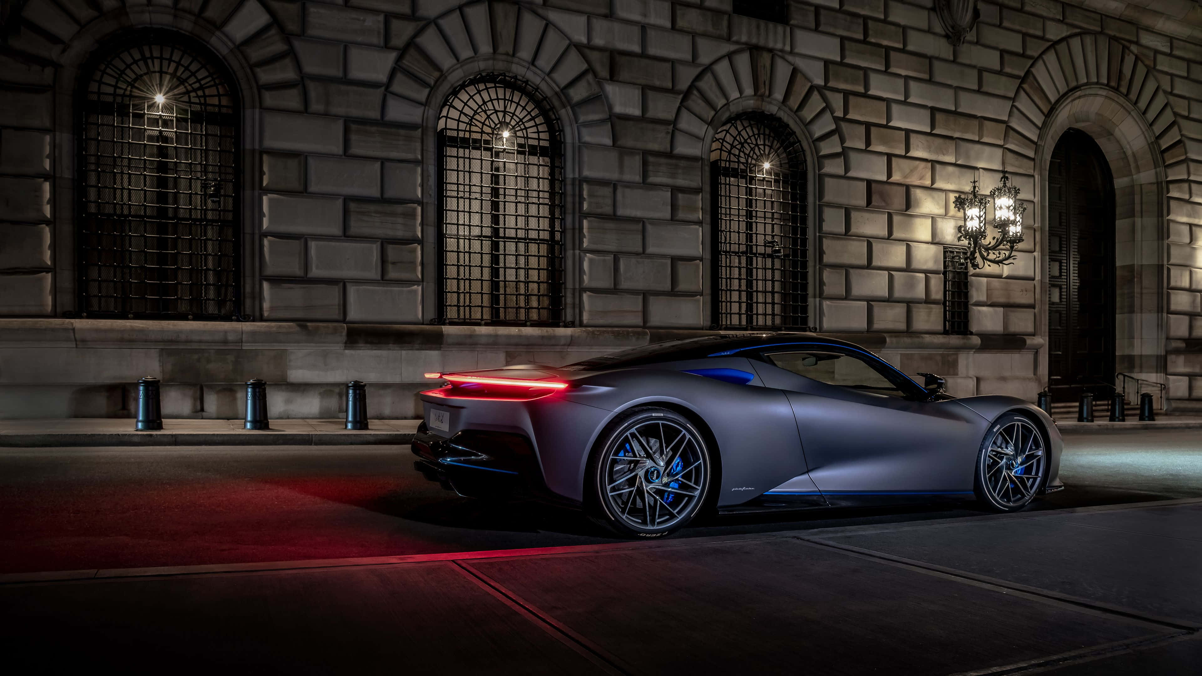 Pininfarina 桌布 壁紙 — 一輛時尚的啞光灰色跑車，帶有發光的紅色尾燈，夜間停在一座帶有拱形窗戶的石頭建築前。