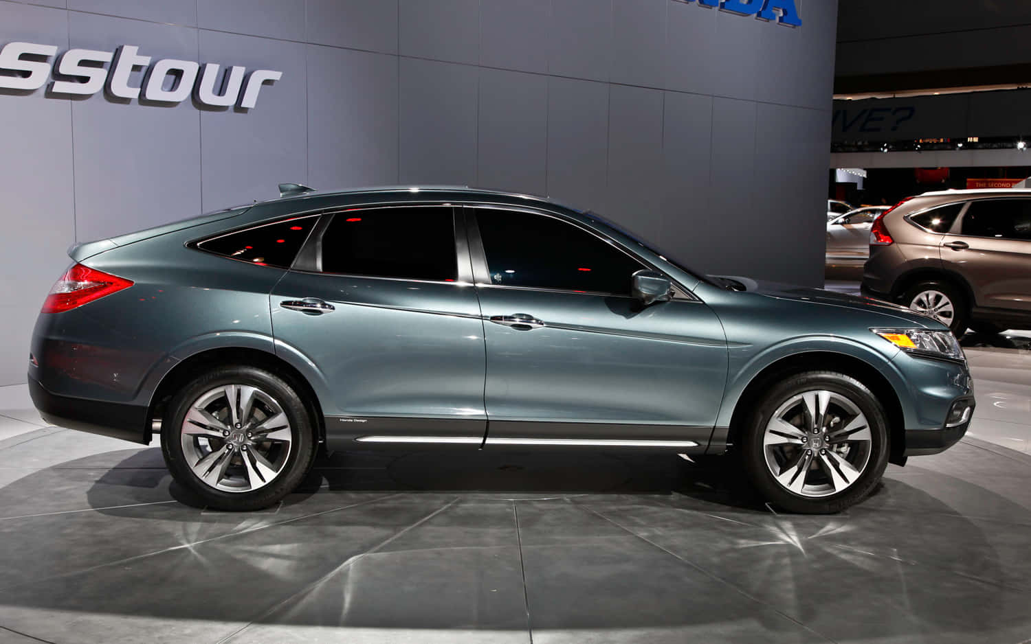 Honda Crosstour 桌布 壁紙 — 一輛時尚金屬青綠色的本田Crosstour房車在車展上展示，地面光滑，燈光明亮，背景帶有品牌標誌。