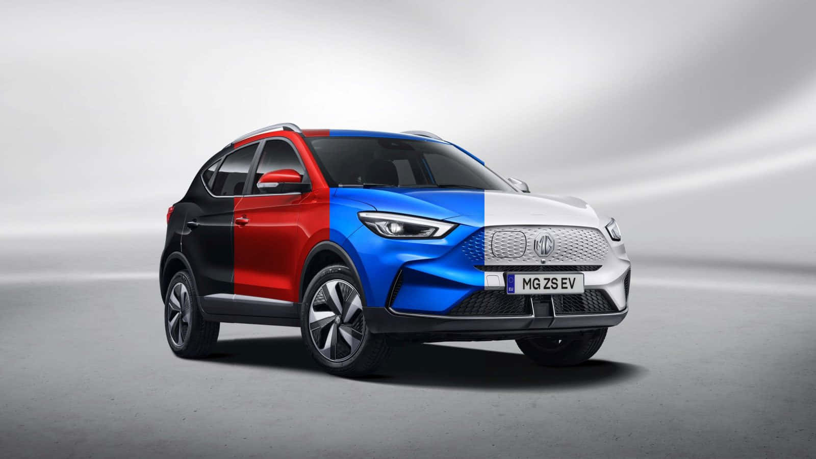  壁紙 — 一部時尚的MG ZS EV SUV，帶有醒目的紅色、藍色和白色面板，在極簡的灰色工作室背景前矗立。