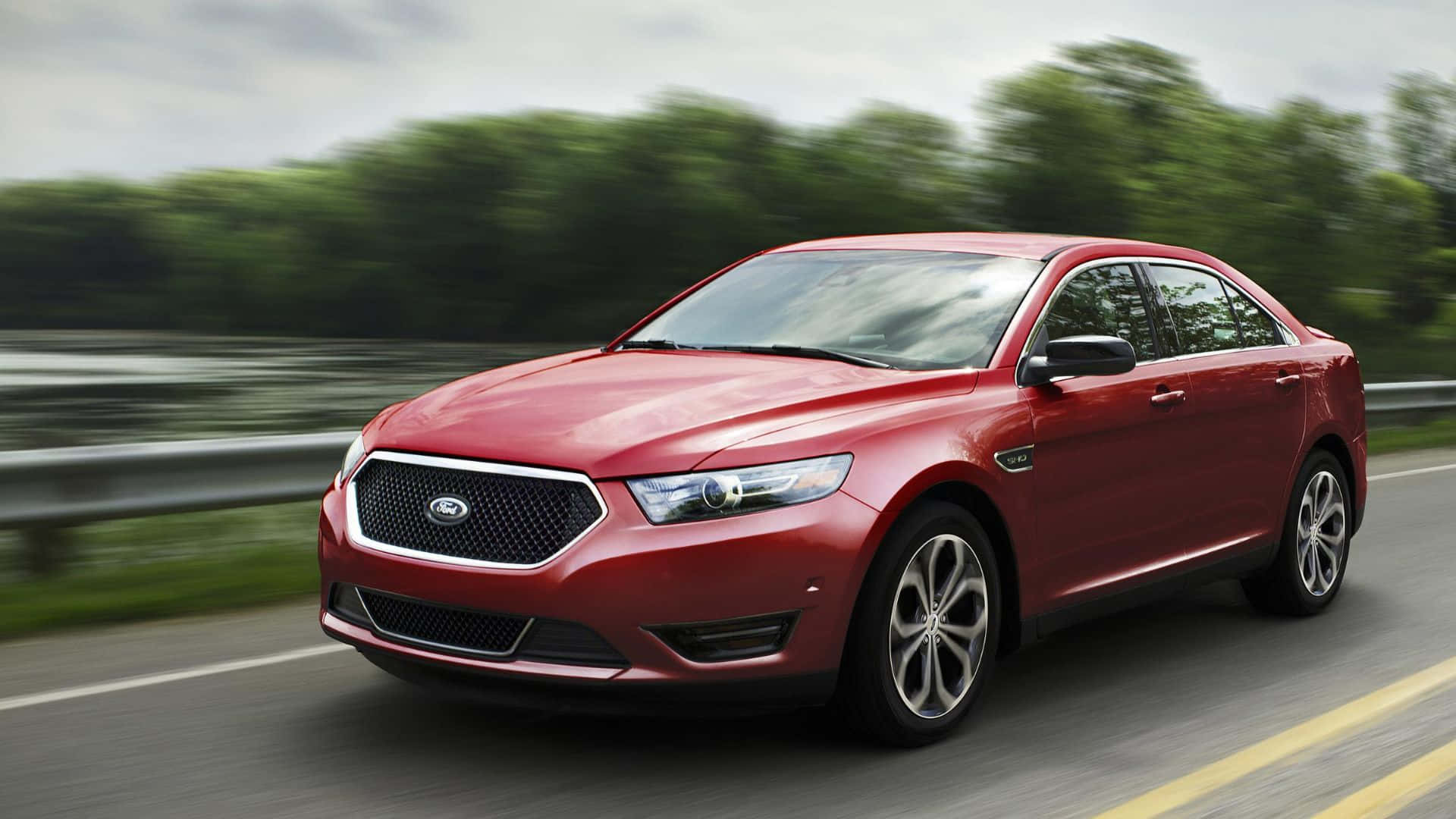 Ford Taurus 桌布 壁紙 — 一輛時尚的紅色福特 Taurus 轎車在高速公路上疾馳，背景是模糊的綠樹和護欄。