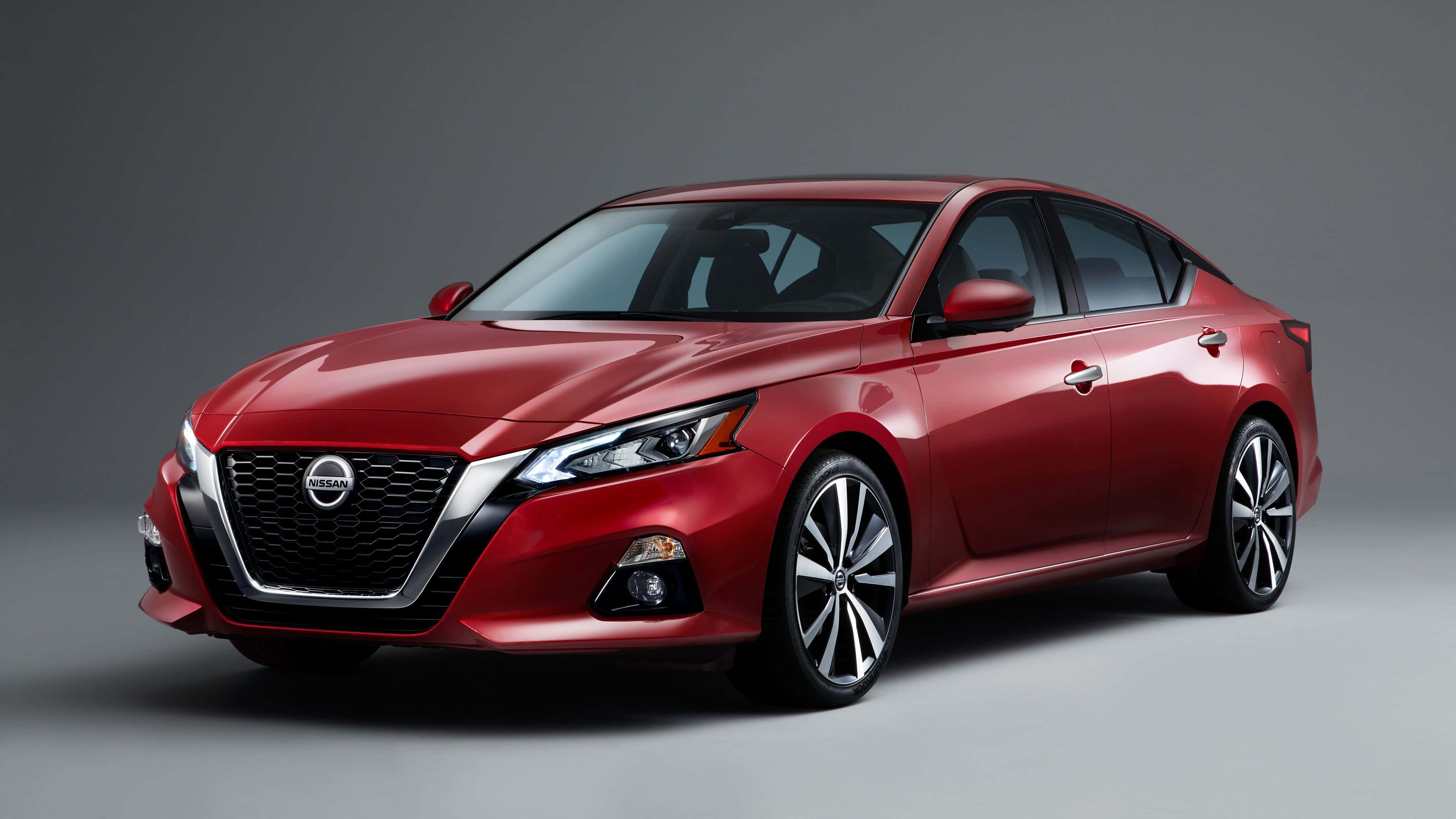 Nissan Altima 桌布 壁紙 — 一輛時尚的紅色日產轎車在攝影棚燈光下，在灰色中性背景前閃閃發光。