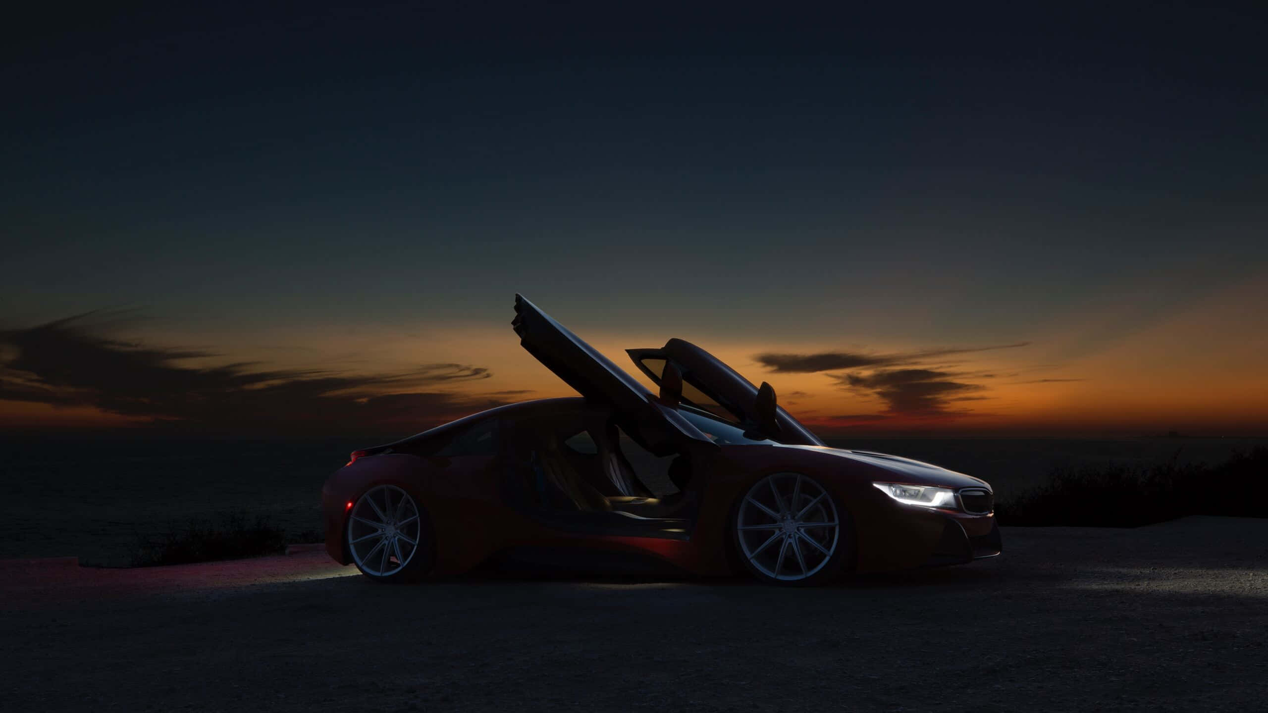 Sunset Drive 桌布 壁紙 — 一架線條流線型的紅色跑車，鷗翼車門打開，停喺懸崖上，喺黃昏時分俯瞰海洋。