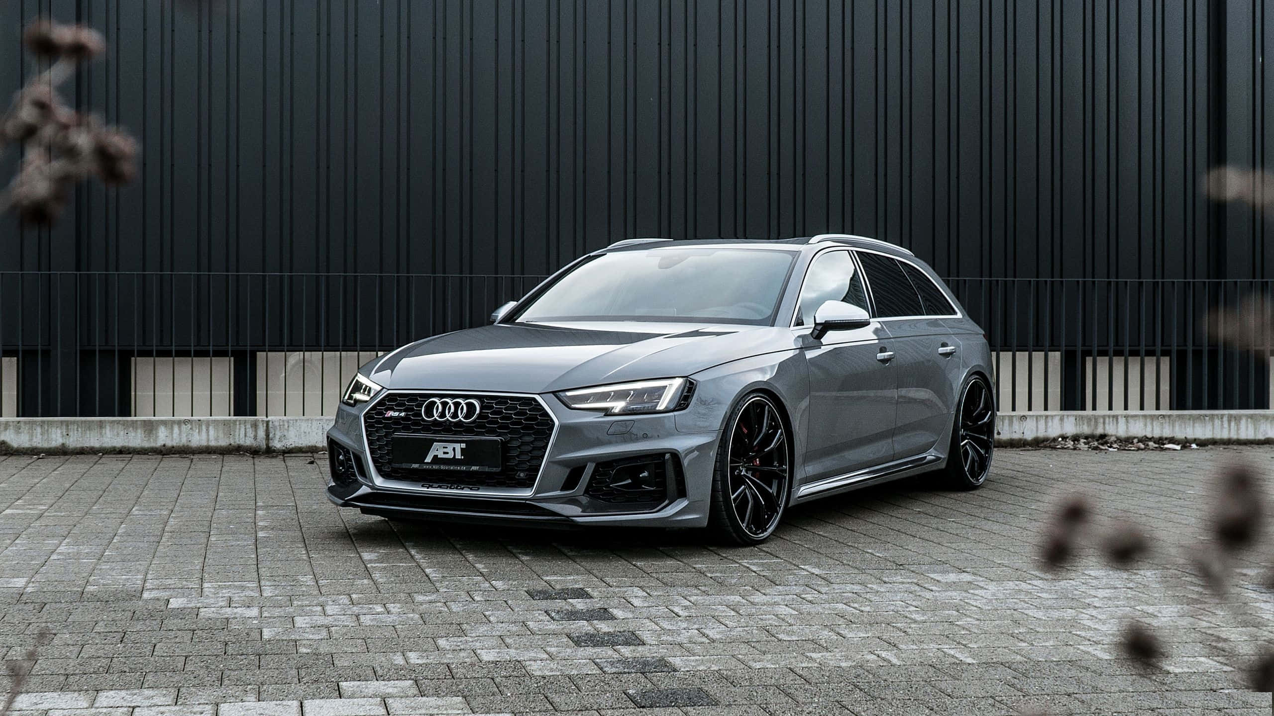 Audi Rs4 桌布 壁紙 — 一架型格銀色ABT改裝奧迪RS4 Avant旅行車停泊在鋪砌的庭院中，背景是深色工業牆。