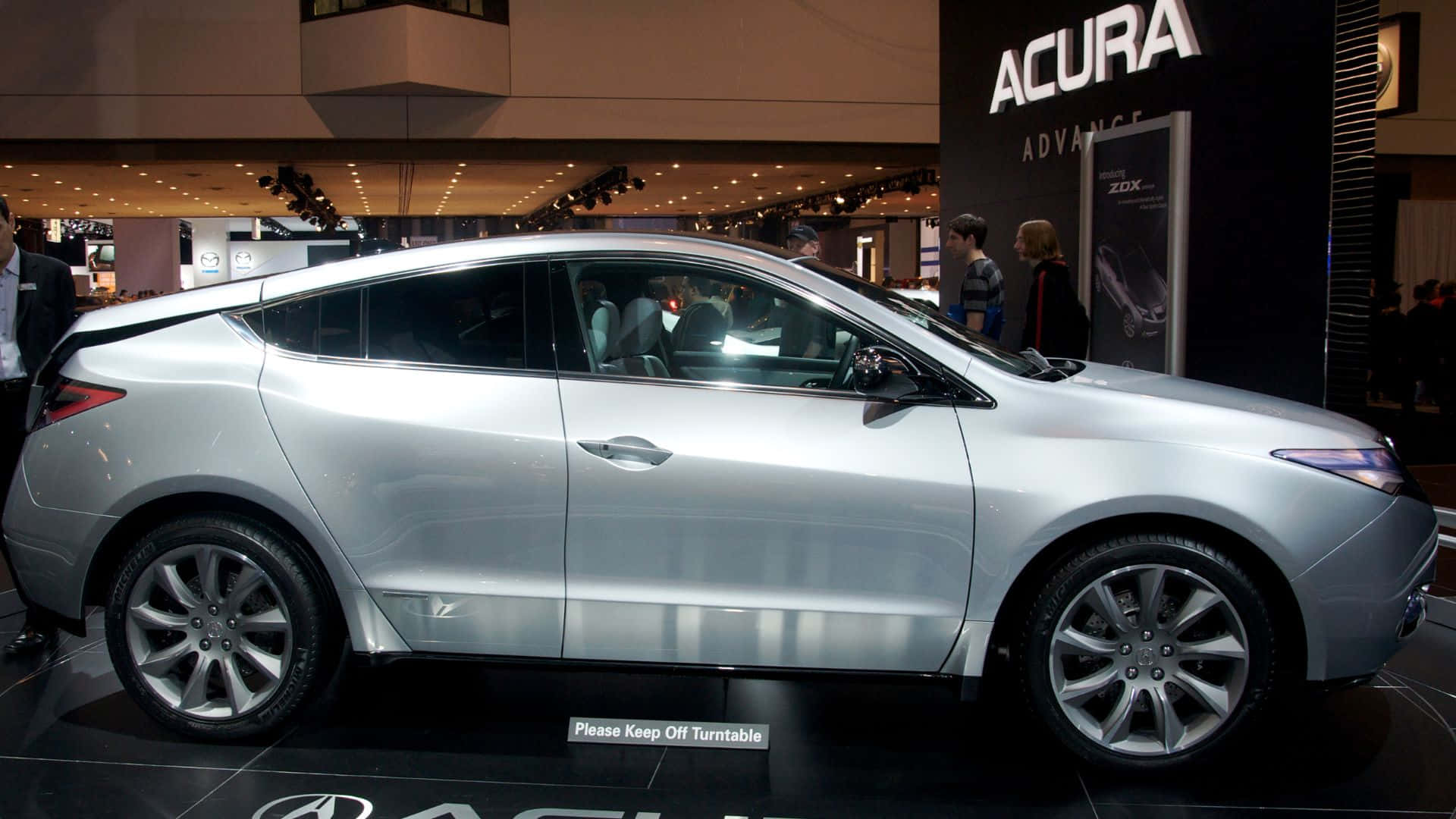 Acura Zdx 桌布 壁紙 — 一輛時尚的銀色Acura ZDX轎跑車在車展上展出，配備拋光輪圈和反光表面，在明亮燈光下閃耀。