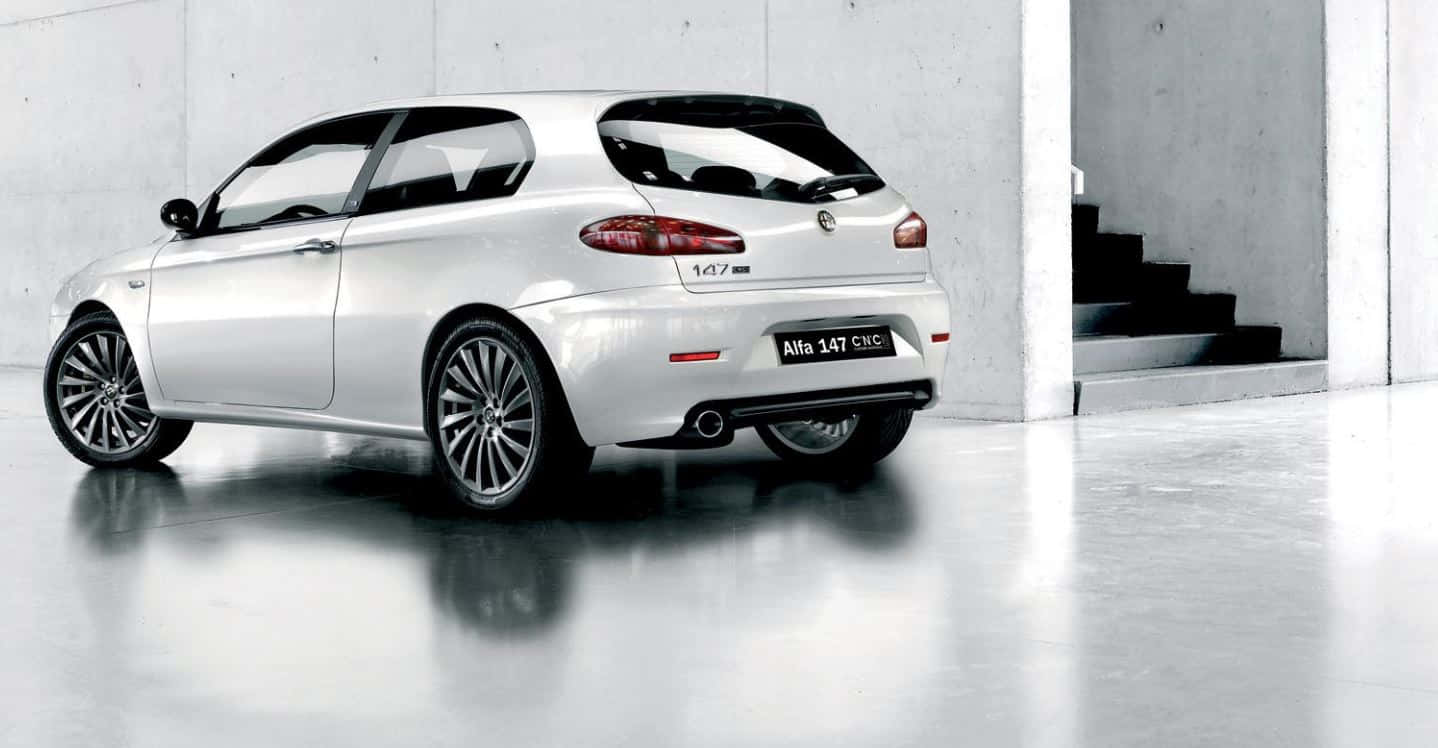Alfa Romeo 147 桌布 壁紙 — 一輛時尚的銀色Alfa 147 GTA跑車在極簡風格的混凝土車庫中展示，配有反光地板和樓梯。