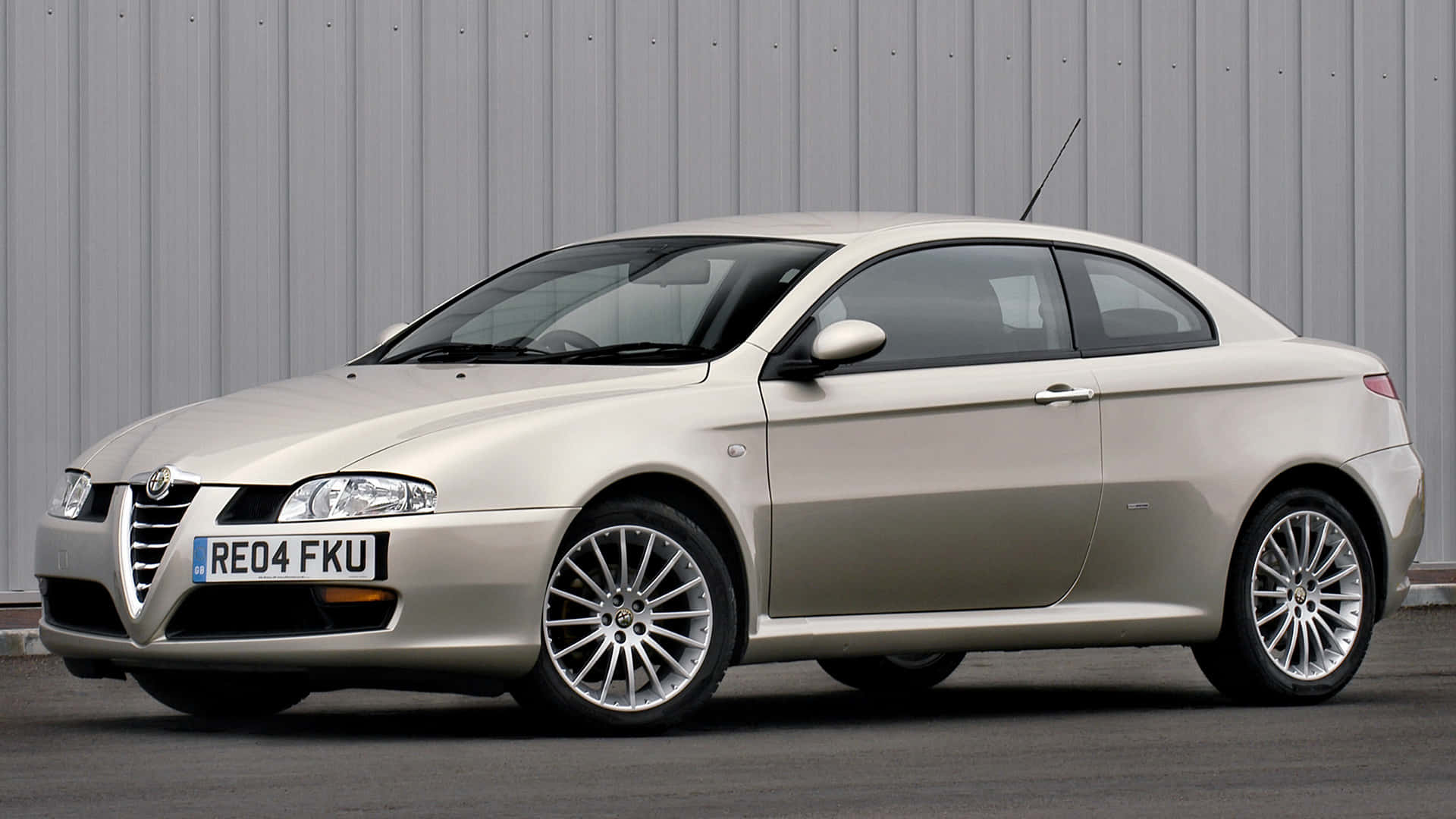 Alfa Romeo Gt 桌布 壁紙 — 一輛時尚的銀色愛快羅密歐雙門跑車停泊在波紋金屬牆旁，配備拋光合金輪圈。