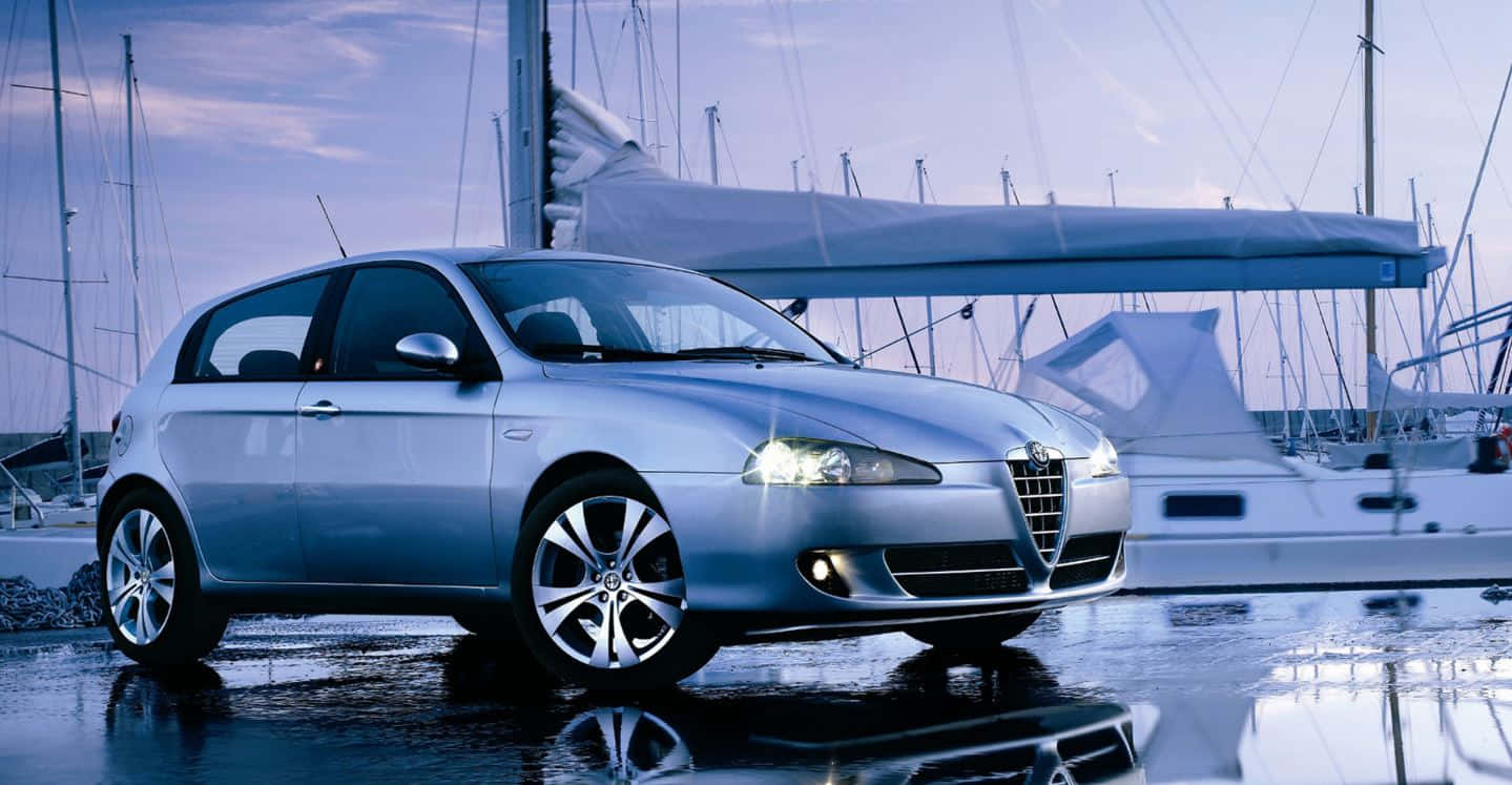 Alfa Romeo 147 桌布 壁紙 — 一架時尚的銀色愛快羅密歐掀背車在暮色天空下的濕滑碼頭旁，在帆船旁邊閃閃發光。