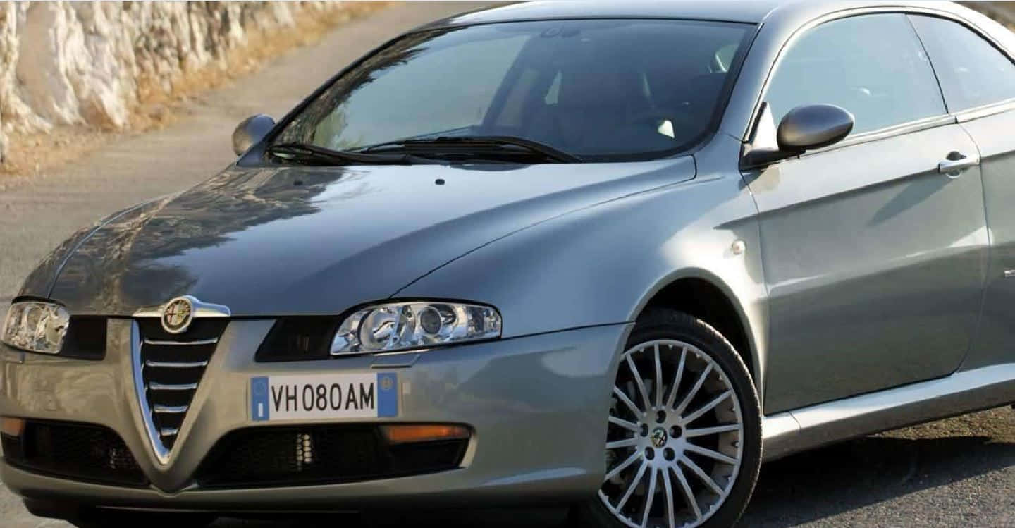 Alfa Romeo Gt 桌布 壁紙 — 一架流線型銀色愛快羅密歐跑車停泊在陽光明媚的鄉村道路上，旁邊是岩石峭壁。
