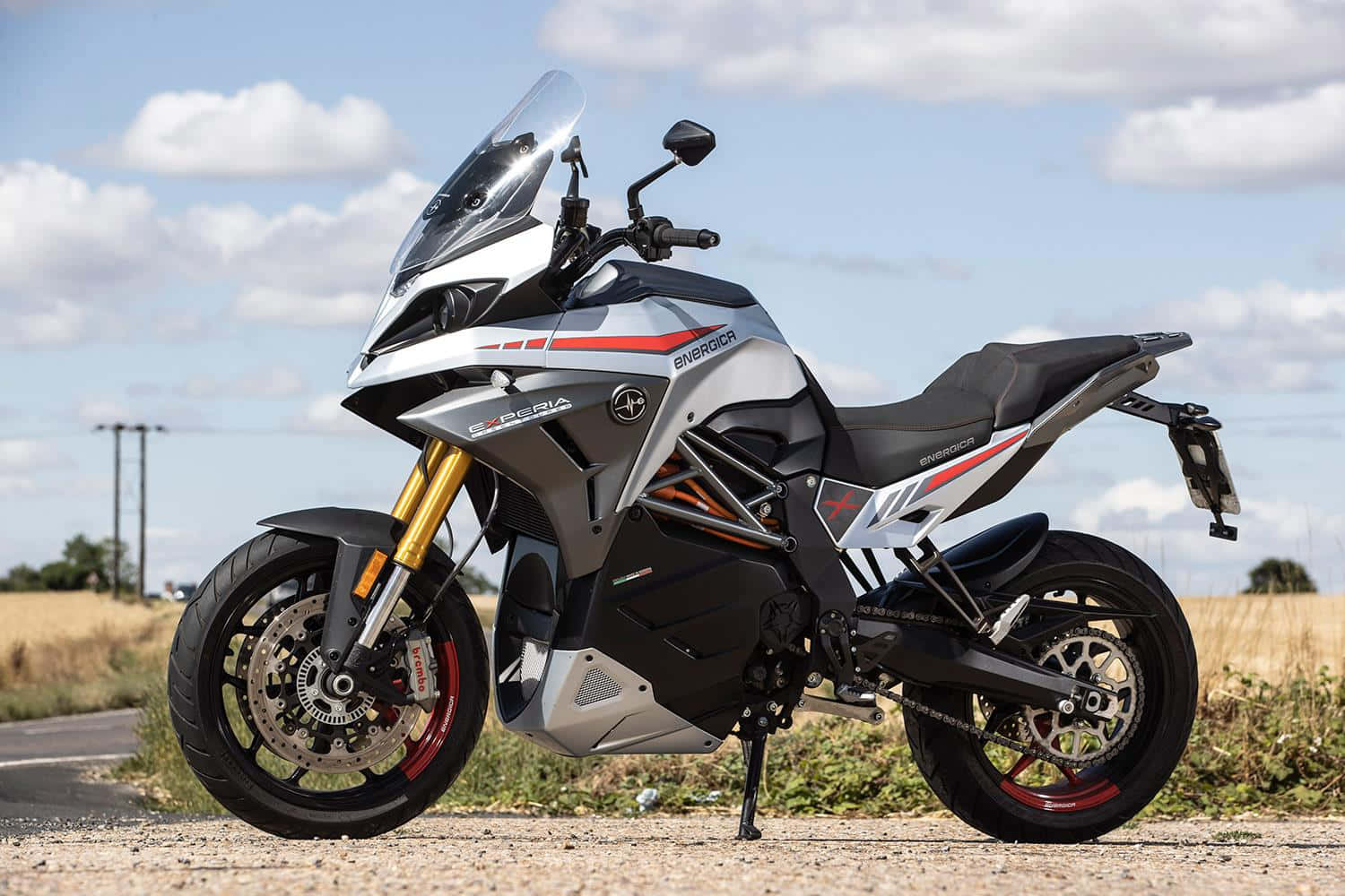  壁紙 — 一架時尚的銀黑色 Energica 電單車，配金色前叉，停泊在碎石路上，天空局部多雲。
