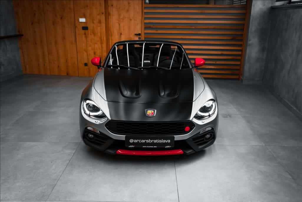 Fiat 124 Spider 桌布 壁紙 — 一輛時尚的銀黑色菲亞特124 Spider，帶有紅色點綴，停放在現代車庫中央，車庫有木門和混凝土地板。