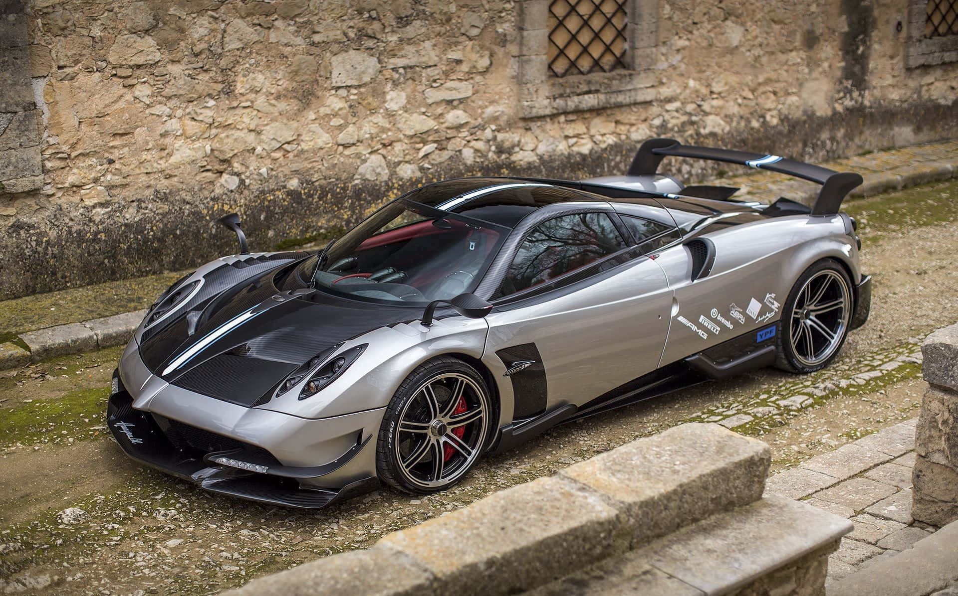 Pagani Huayra Bc 桌布 壁紙 — 一架時尚的銀黑色超跑停泊在鵝卵石街道上，旁邊是風化的石牆。