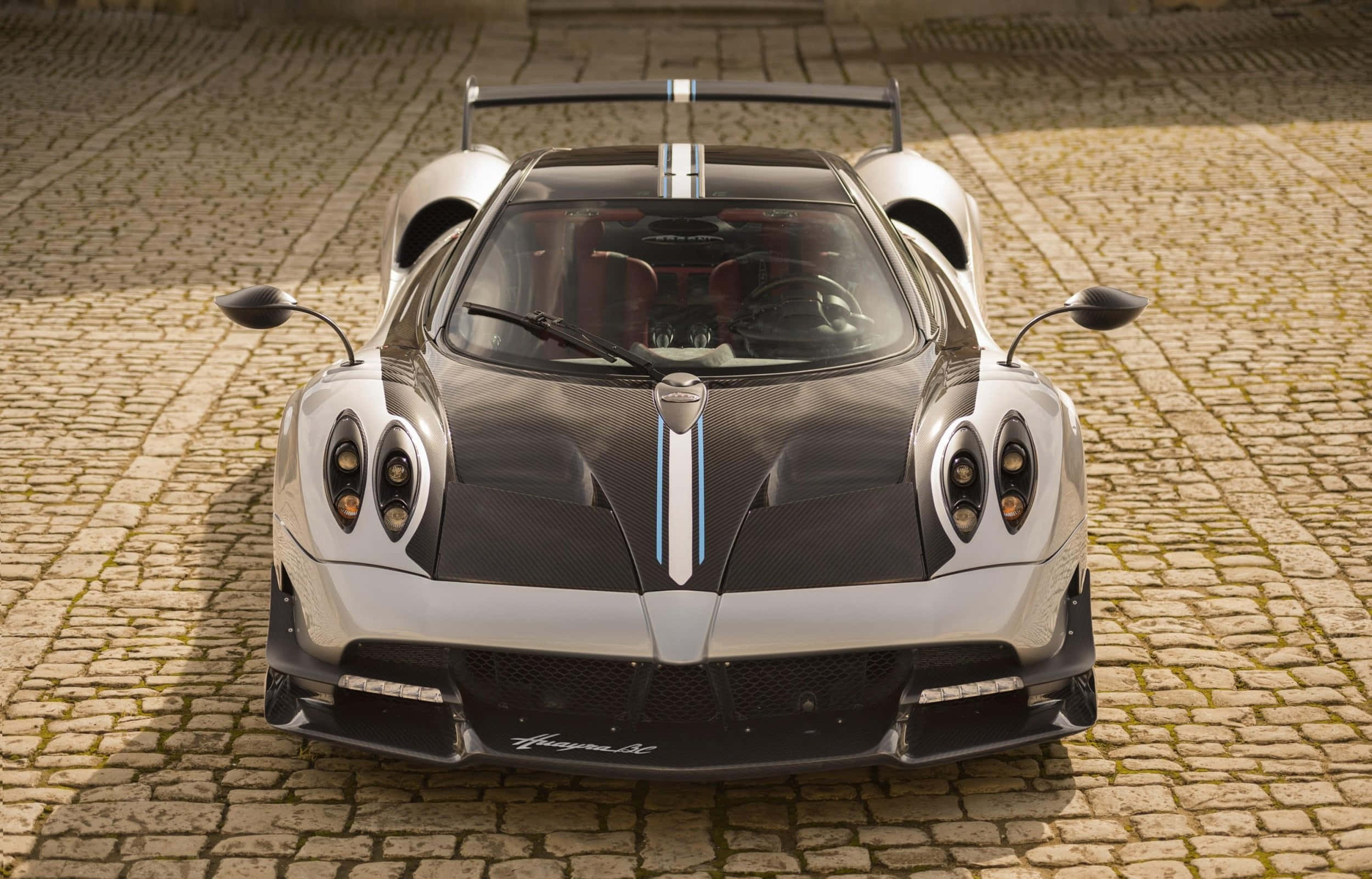 Pagani Huayra Roadster Bc 桌布 壁紙 — 一輛帶有藍色條紋的時尚銀黑 Pagani Huayra BC 超級跑車，停在陽光普照的鵝卵石街道中央。