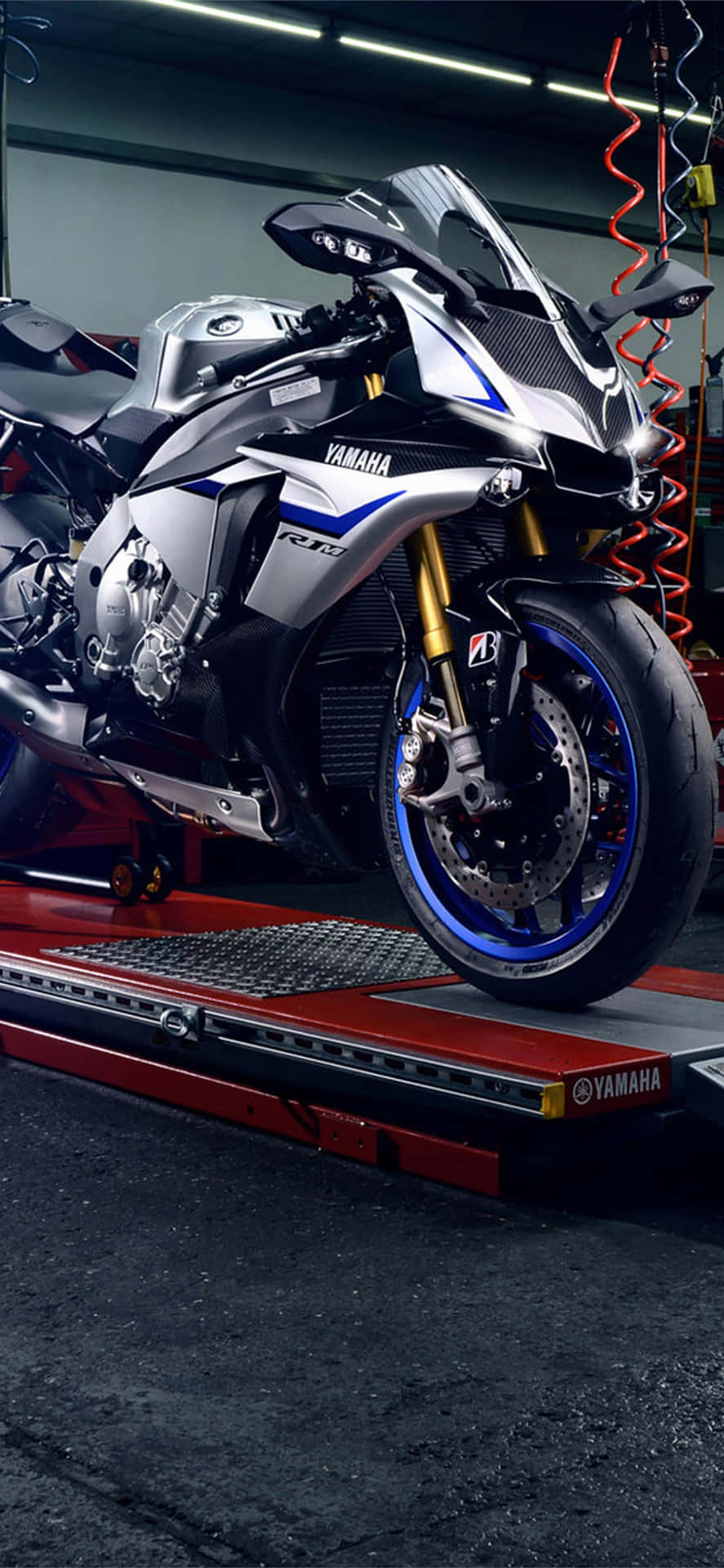  壁紙 — 一架流線型的銀藍色Yamaha R1電單車在車庫明亮的燈光下，在紅色升降台上閃閃發光。