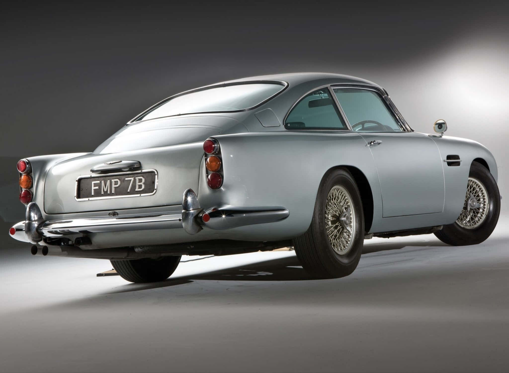Aston Martin Db5 桌布 壁紙 — 一輛流線型的銀色Aston Martin DB5在攝影棚燈光下閃耀，展現其標誌性曲線和鍍鉻細節。