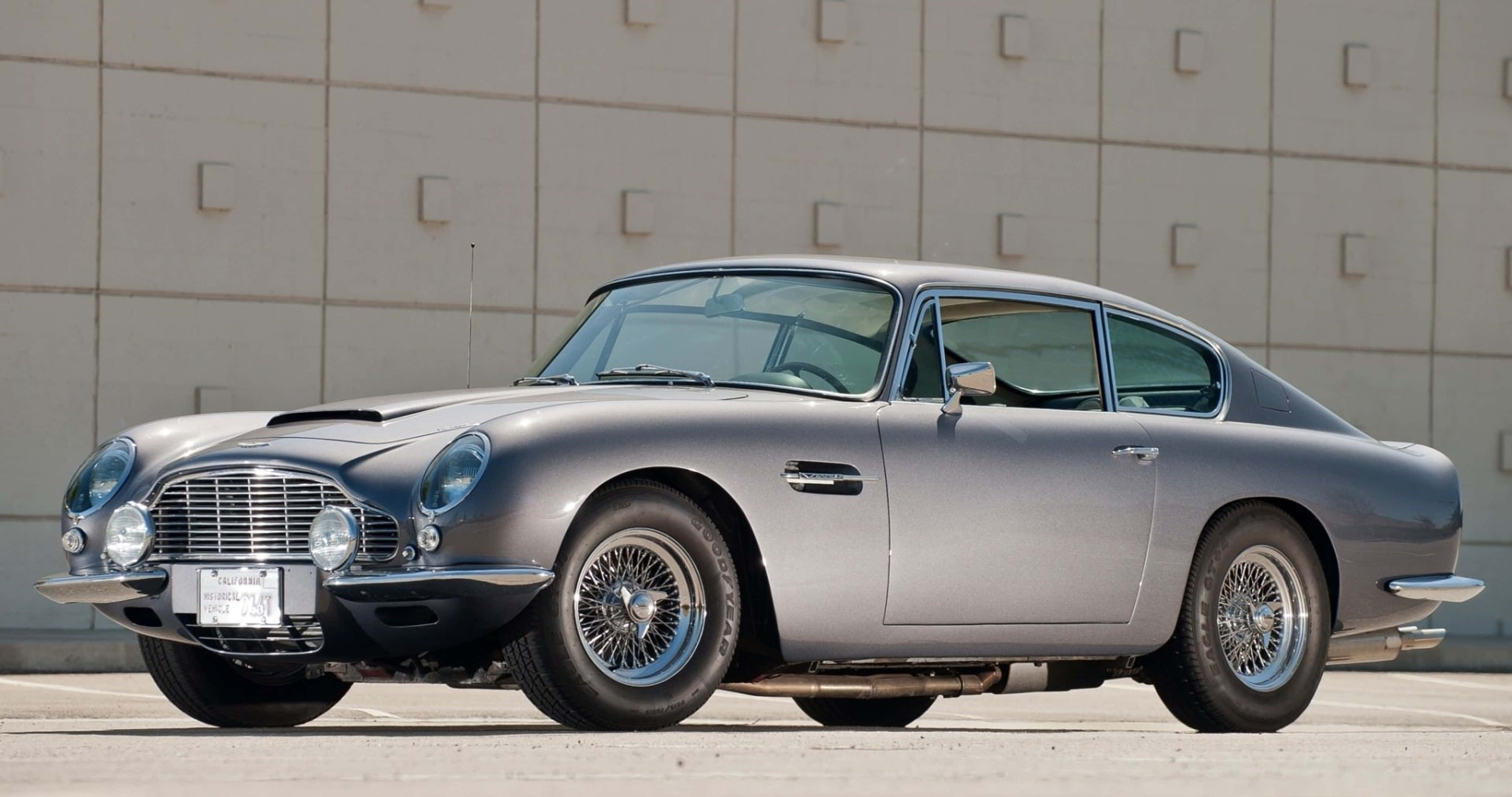 Aston Martin Db5 桌布 壁紙 — 一架流線型銀色Aston Martin DB5在明亮日光下閃耀，停泊在簡約混凝土牆前。