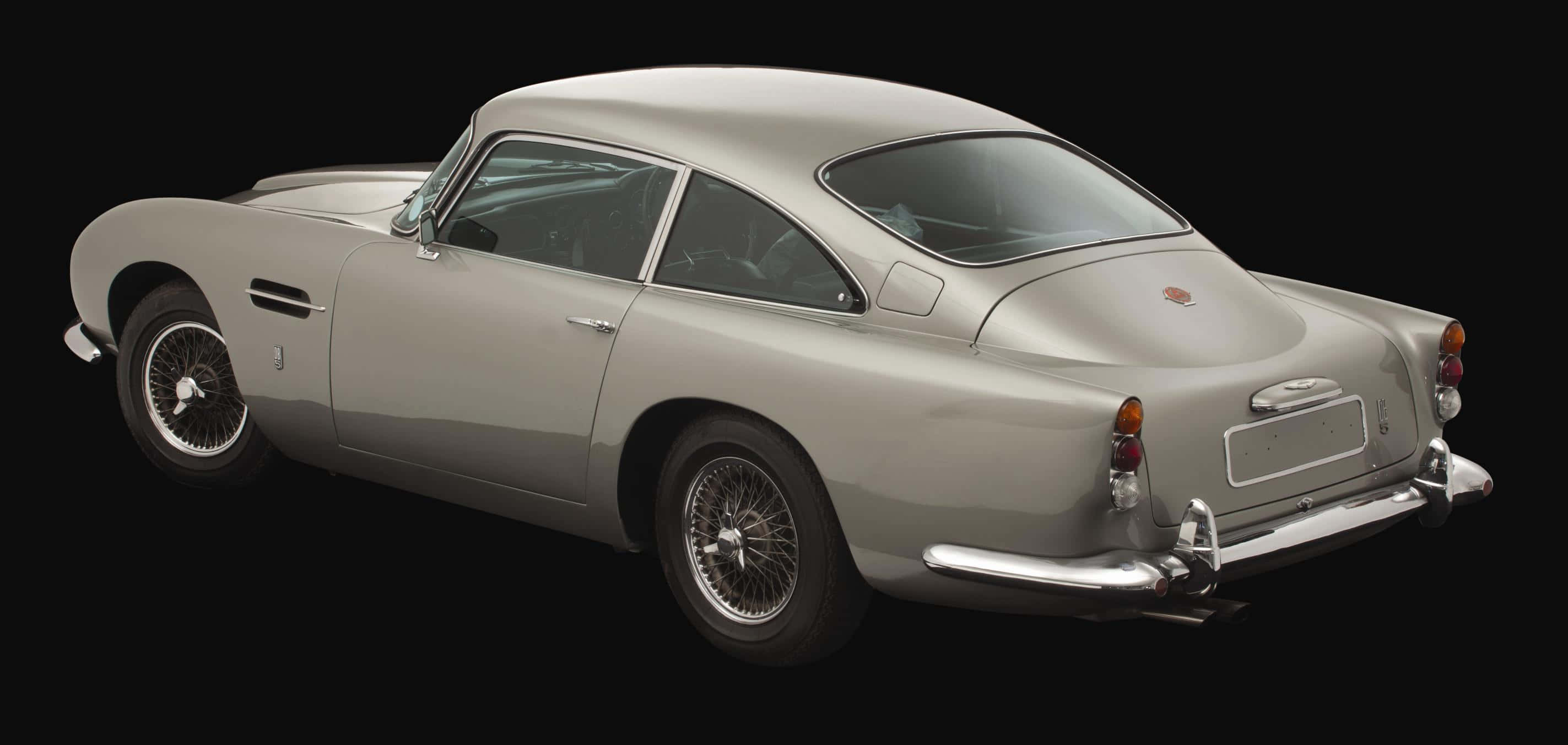 Aston Martin Db5 桌布 壁紙 — 一輛流線型的銀色Aston Martin DB5以側面輪廓展示在黑色背景上，突出其經典曲線和鍍鉻細節。