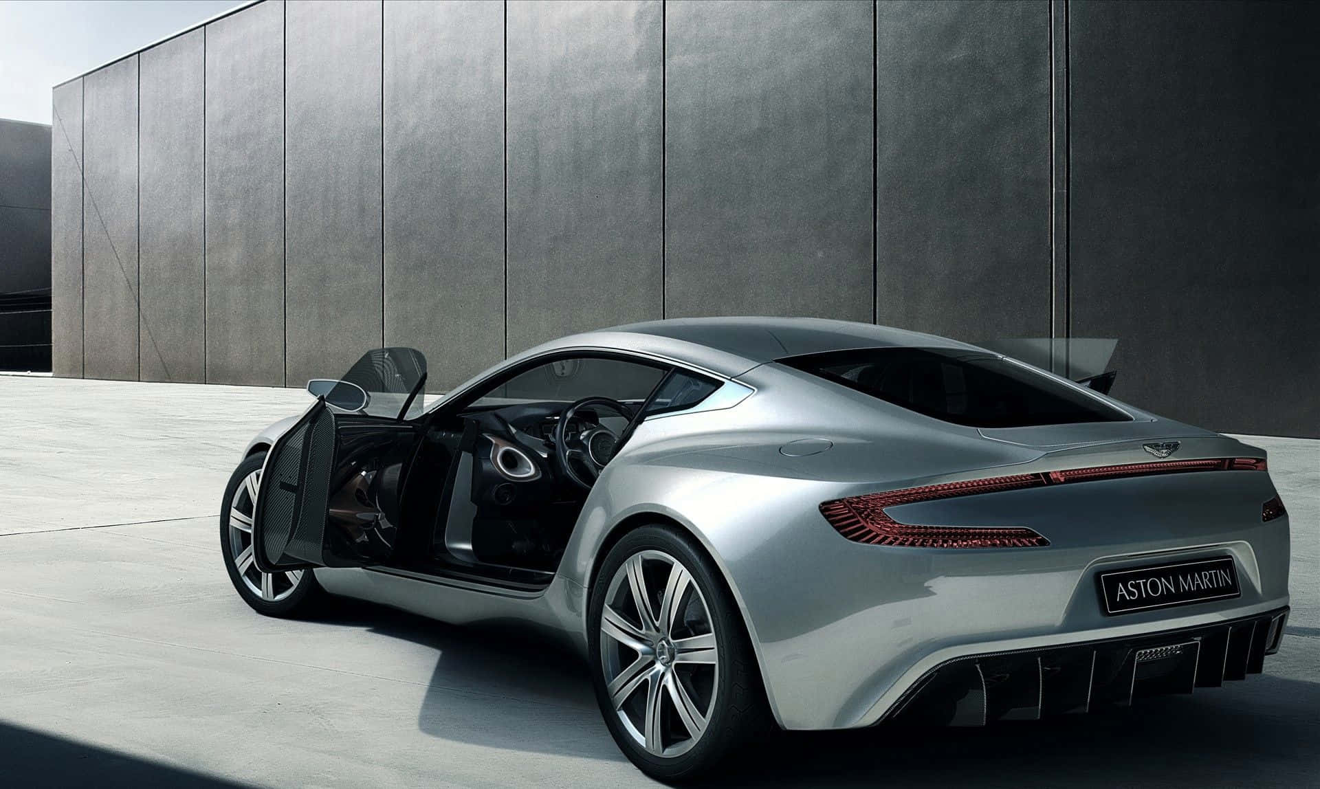 Aston Martin One-77 桌布 壁紙 — 一架時尚的銀色Aston Martin跑車，打開鷗翼車門，停泊在簡約灰色混凝土牆前。