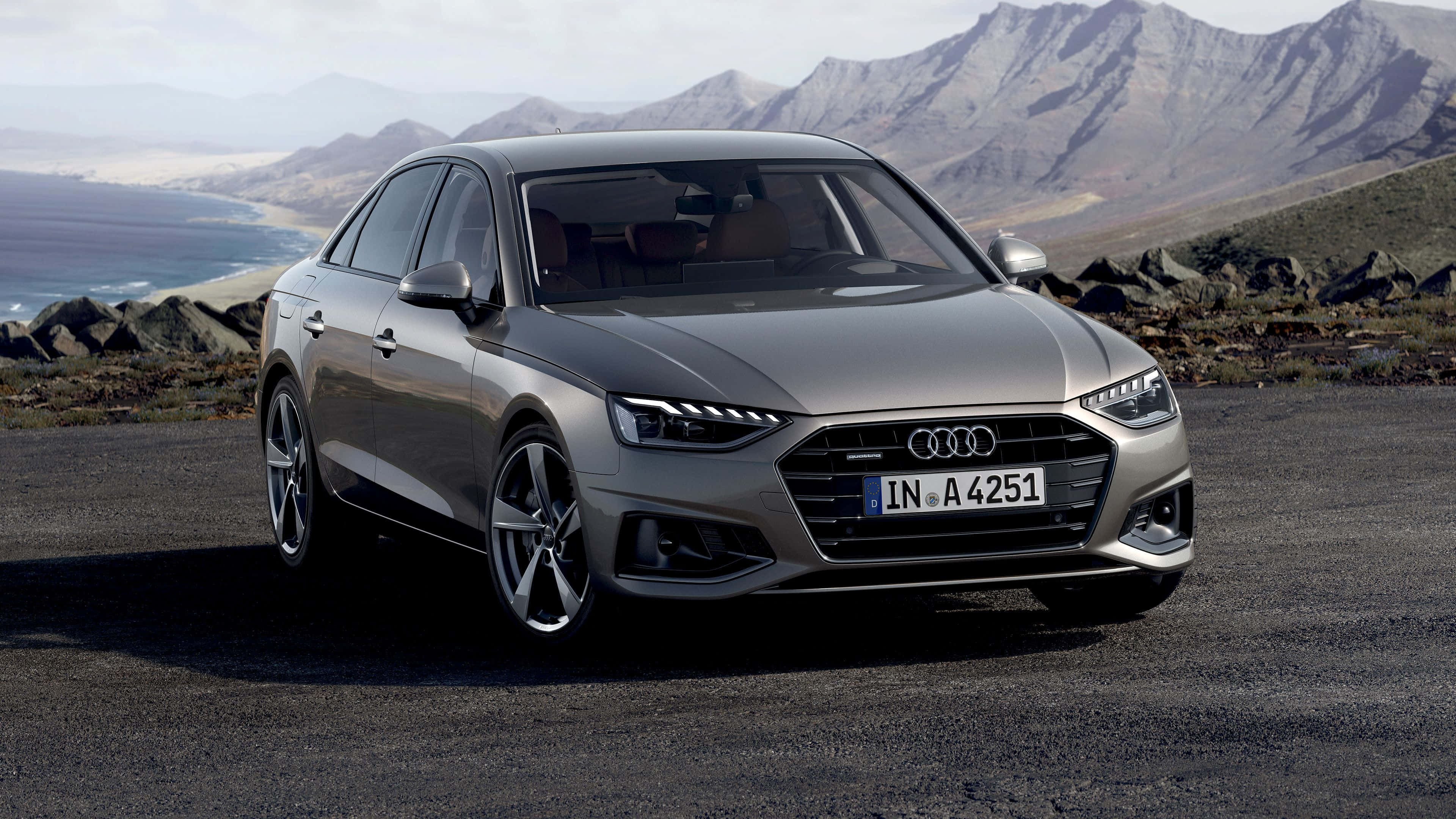 Audi A4 桌布 壁紙 — 一輛時尚的銀色奧迪A4轎車停泊在碎石路上，背景是崎嶇的山脈和遠處的湖泊。
