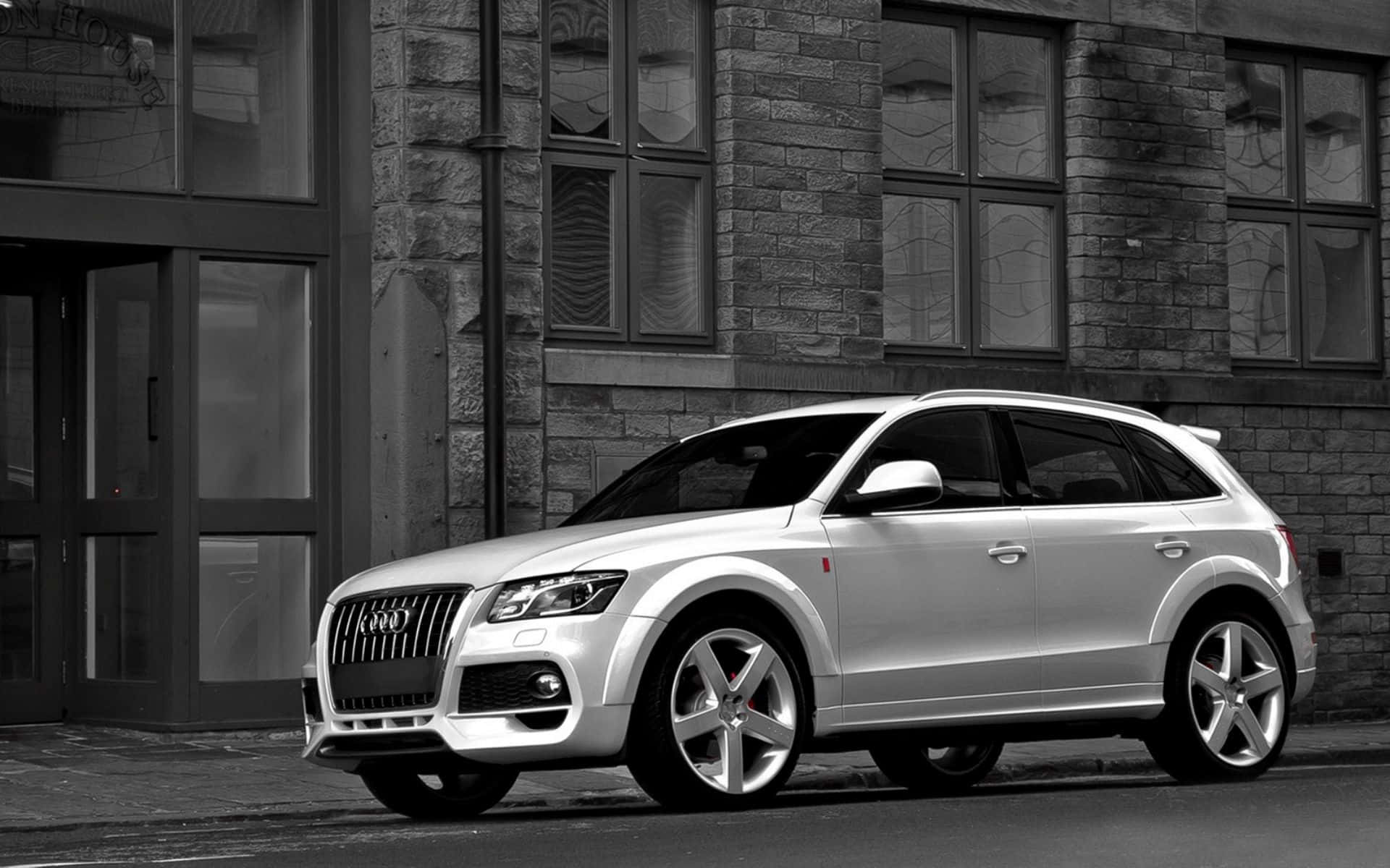 Audi Q5 桌布 壁紙 — 一架型格銀色Audi Q7 SUV停泊在城巿街道旁的石建築物旁邊，以單色呈現。