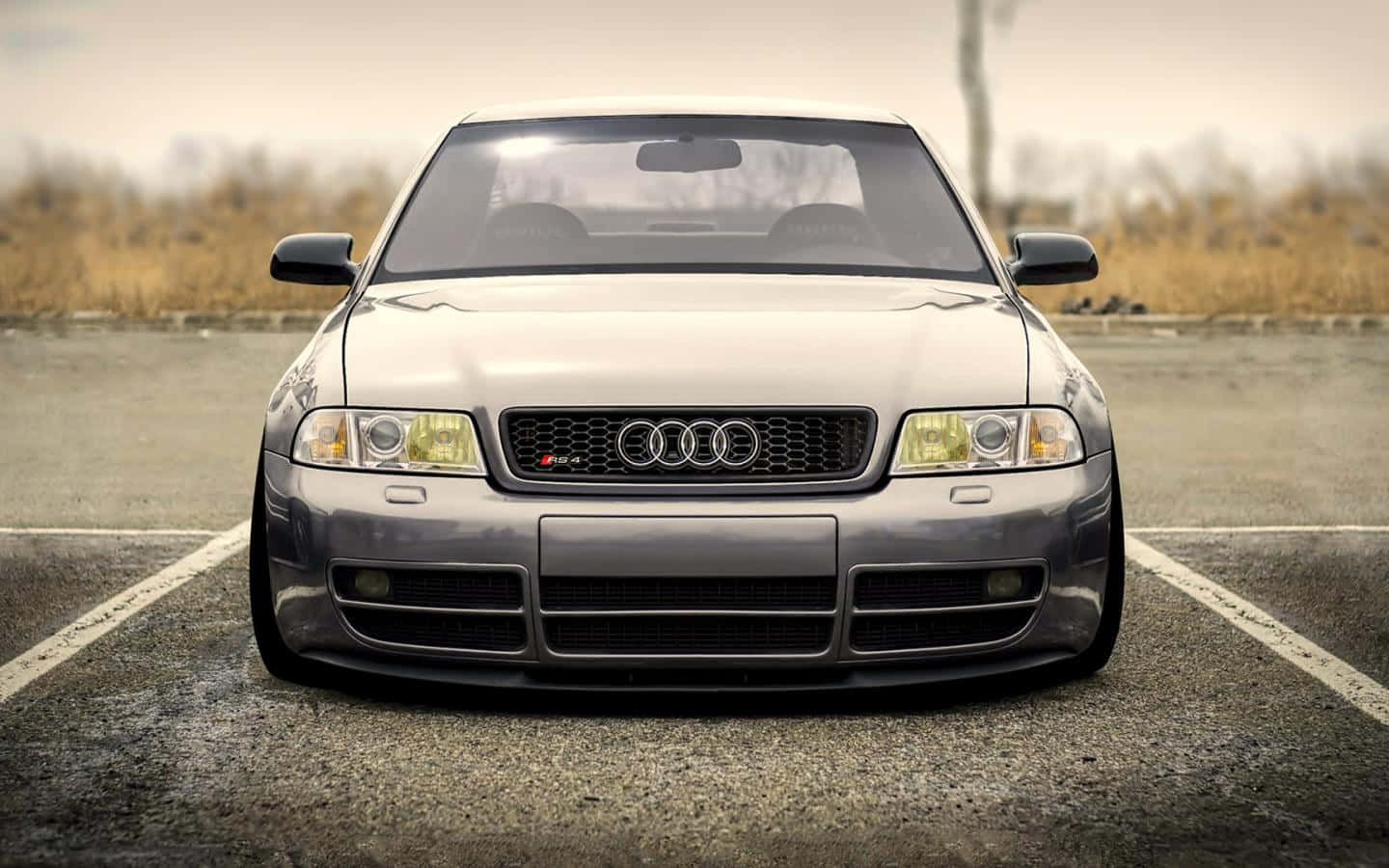 Audi Rs5 桌布 壁紙 — 一架型格銀色奧迪跑車，降低懸掛，停泊在空曠的瀝青場地上，天空多雲。