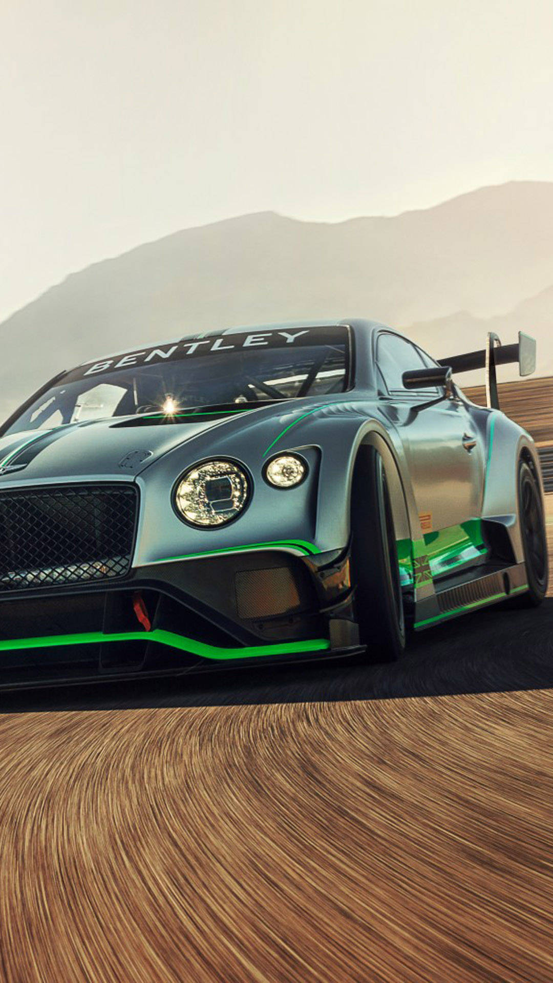 銀色 Bentley 賽車在賽道上奔馳，帶有動態模糊和山巒背景。
