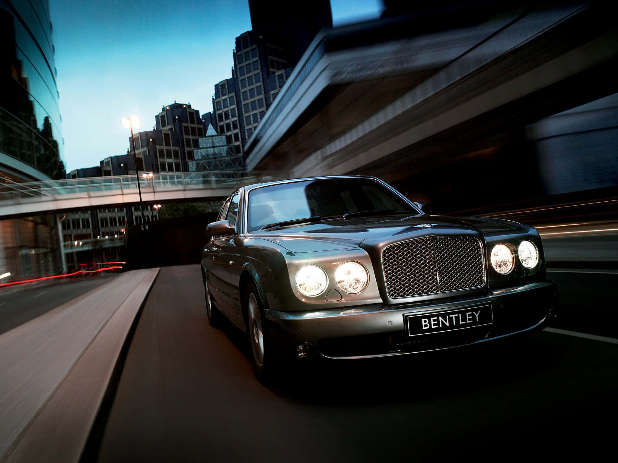 Bentley Arnage 桌布 壁紙 — 一輛流線型銀色賓利在暮色中的城市隧道內高速飛馳，模糊的城市燈光掠過。
