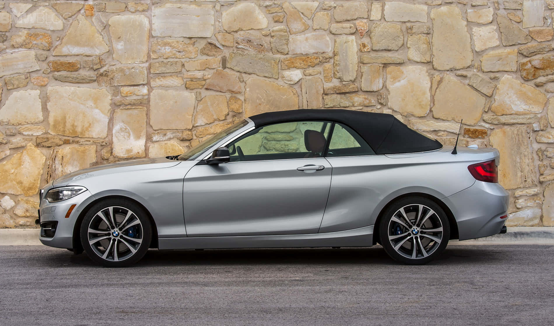 Bmw 2 Series 桌布 壁紙 — 一架時尚的銀色寶馬開篷車，配黑色軟頂，停泊在質樸的石牆旁。