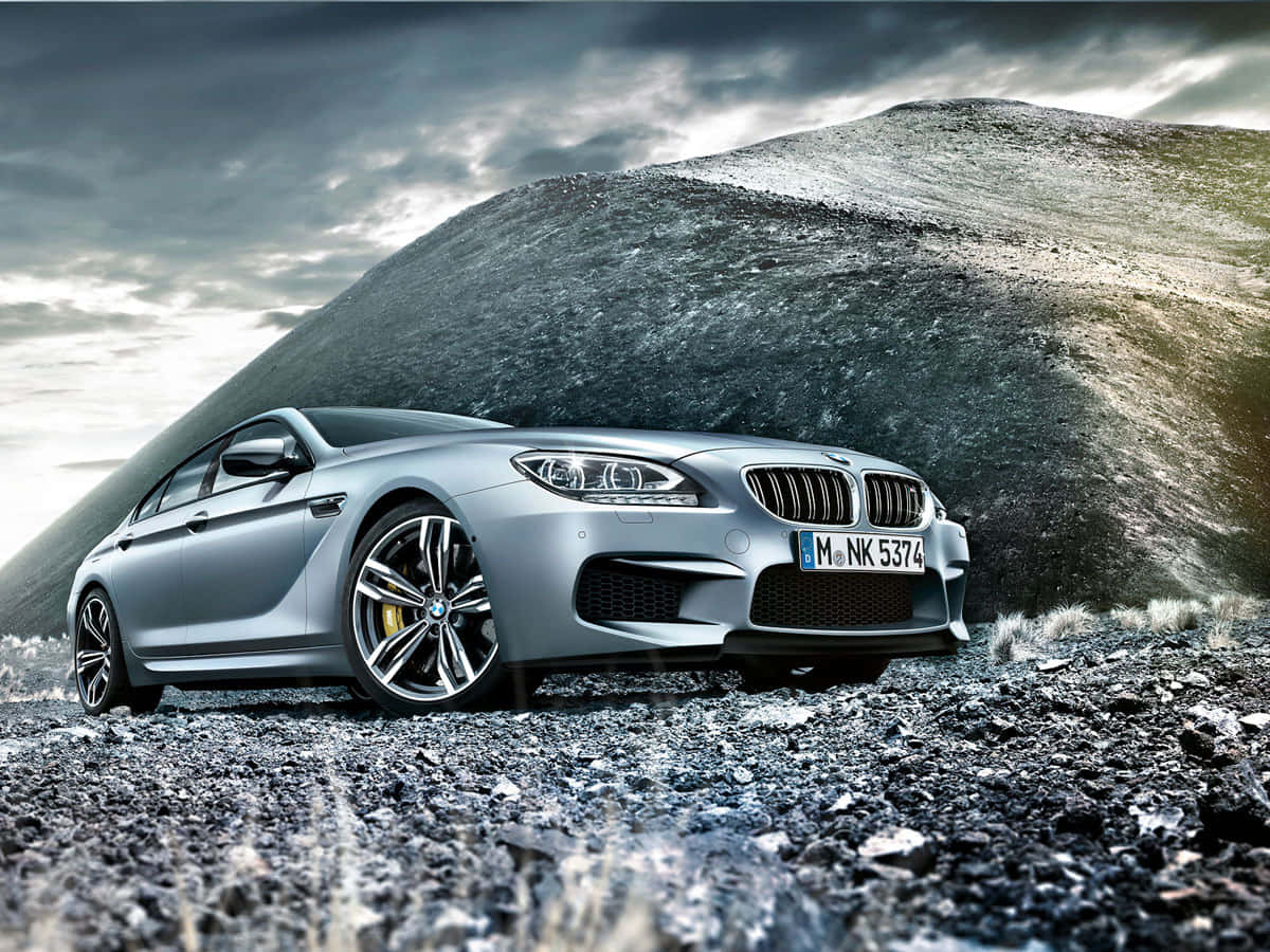 Bmw M6 桌布 壁紙 — 一架流線型銀色BMW M6跑車停泊在岩石地形上，背後有巨大的黑暗山丘，天空風暴密佈。